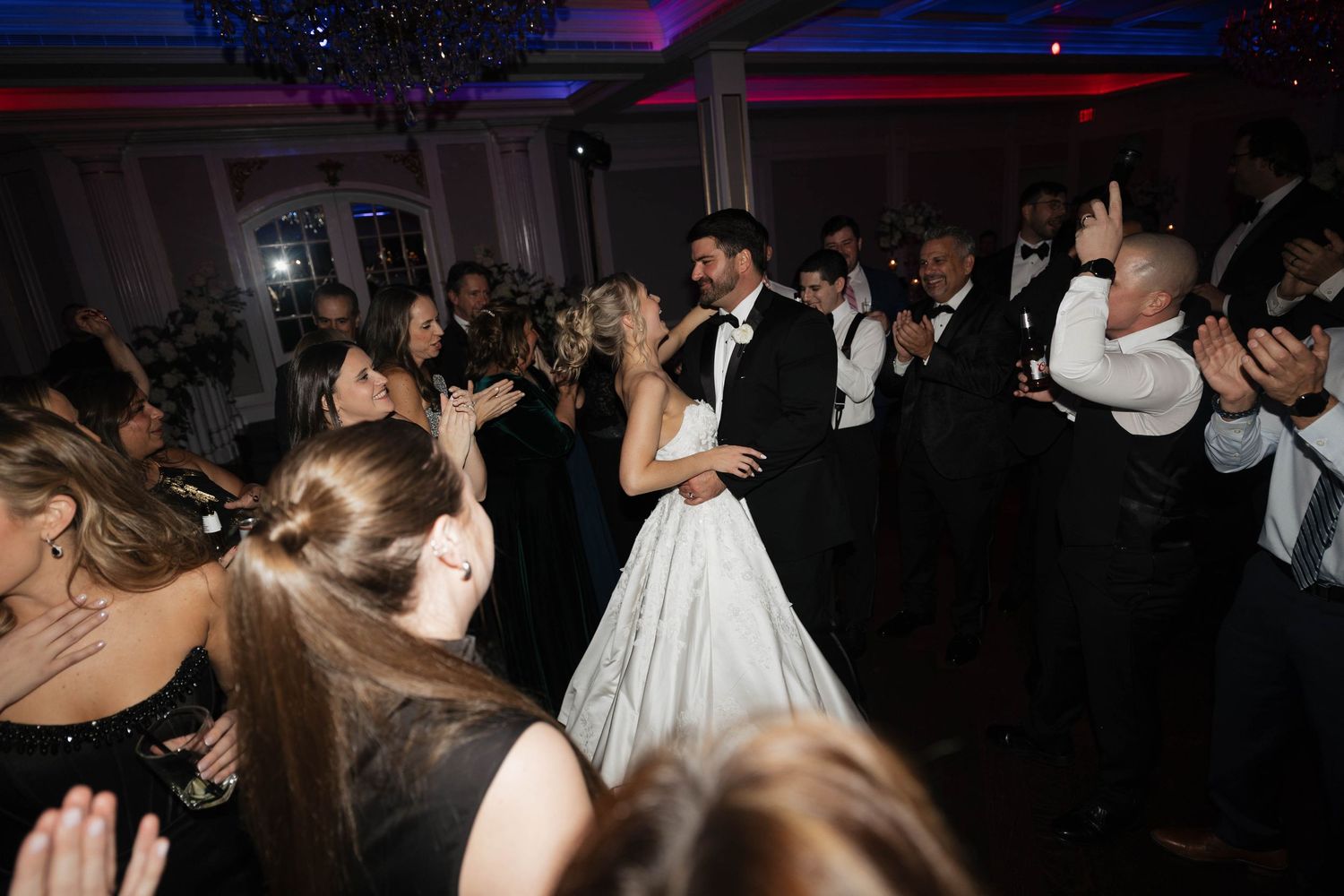 Wedding reception dance floor packed with celebrating guests under blue accent lights.