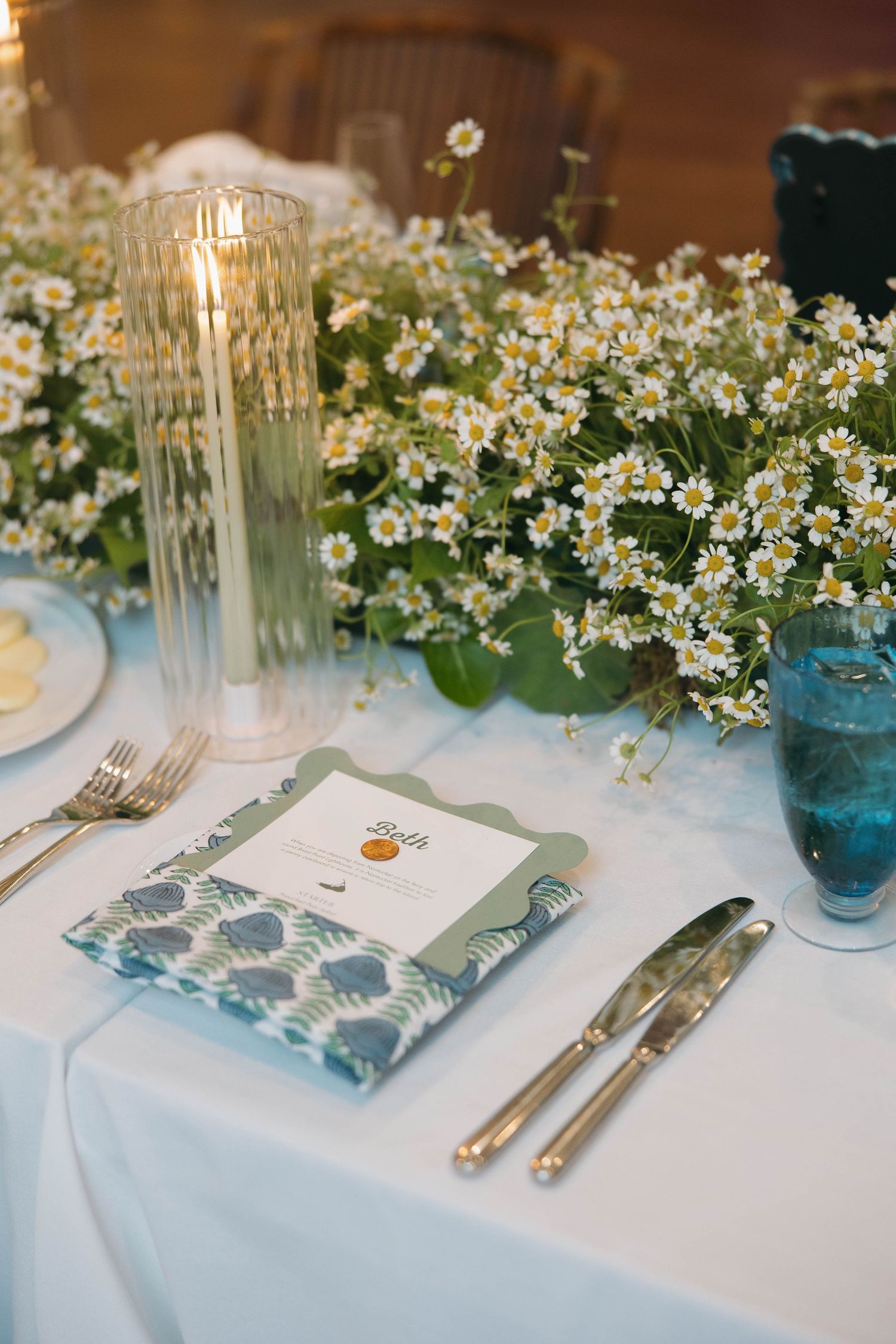 White and blue table settings with delicate floral arrangements and patterned napkins for a wedding reception.