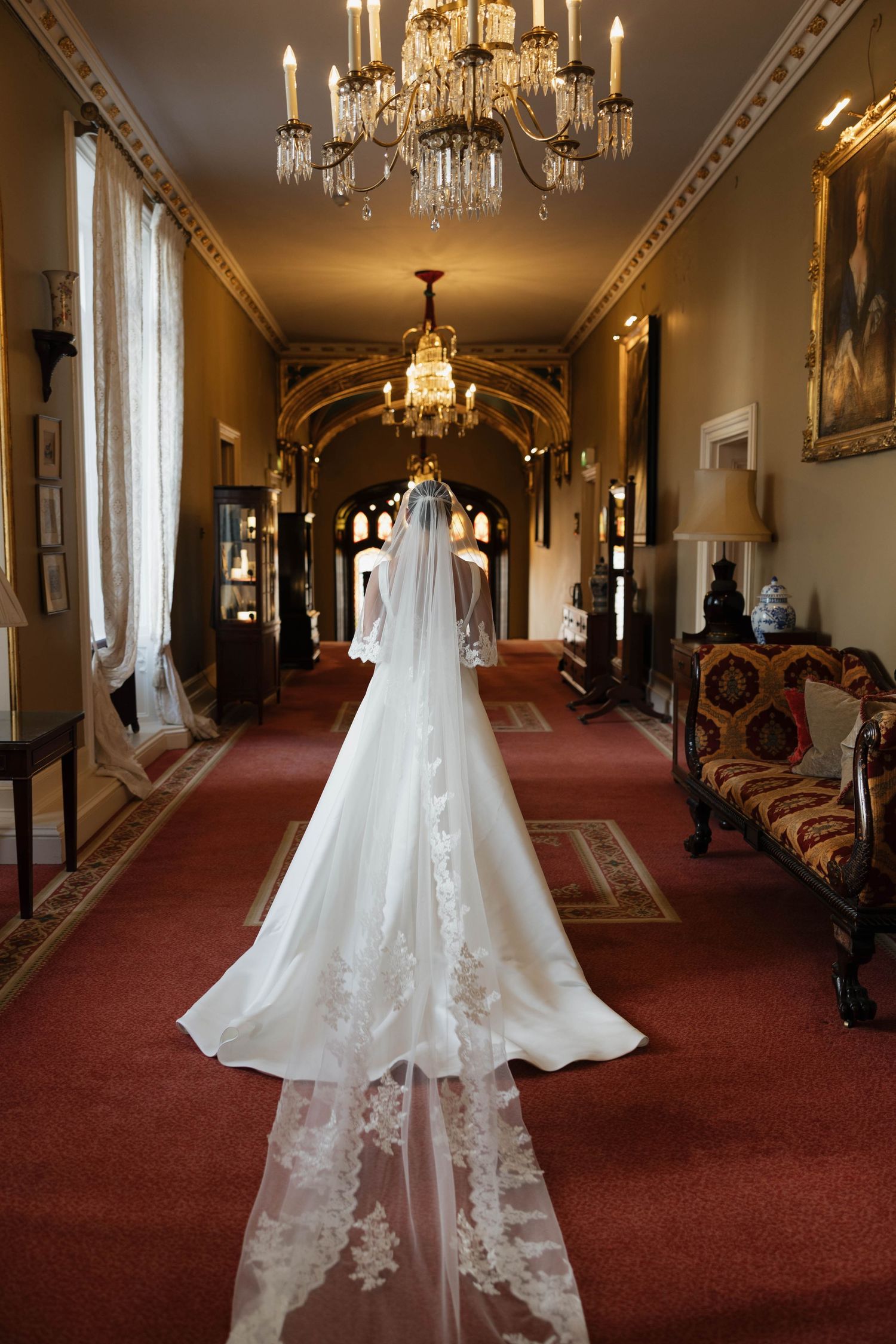 Wedding dress displayed in elegant hallway with crystal chandeliers and red carpet.
