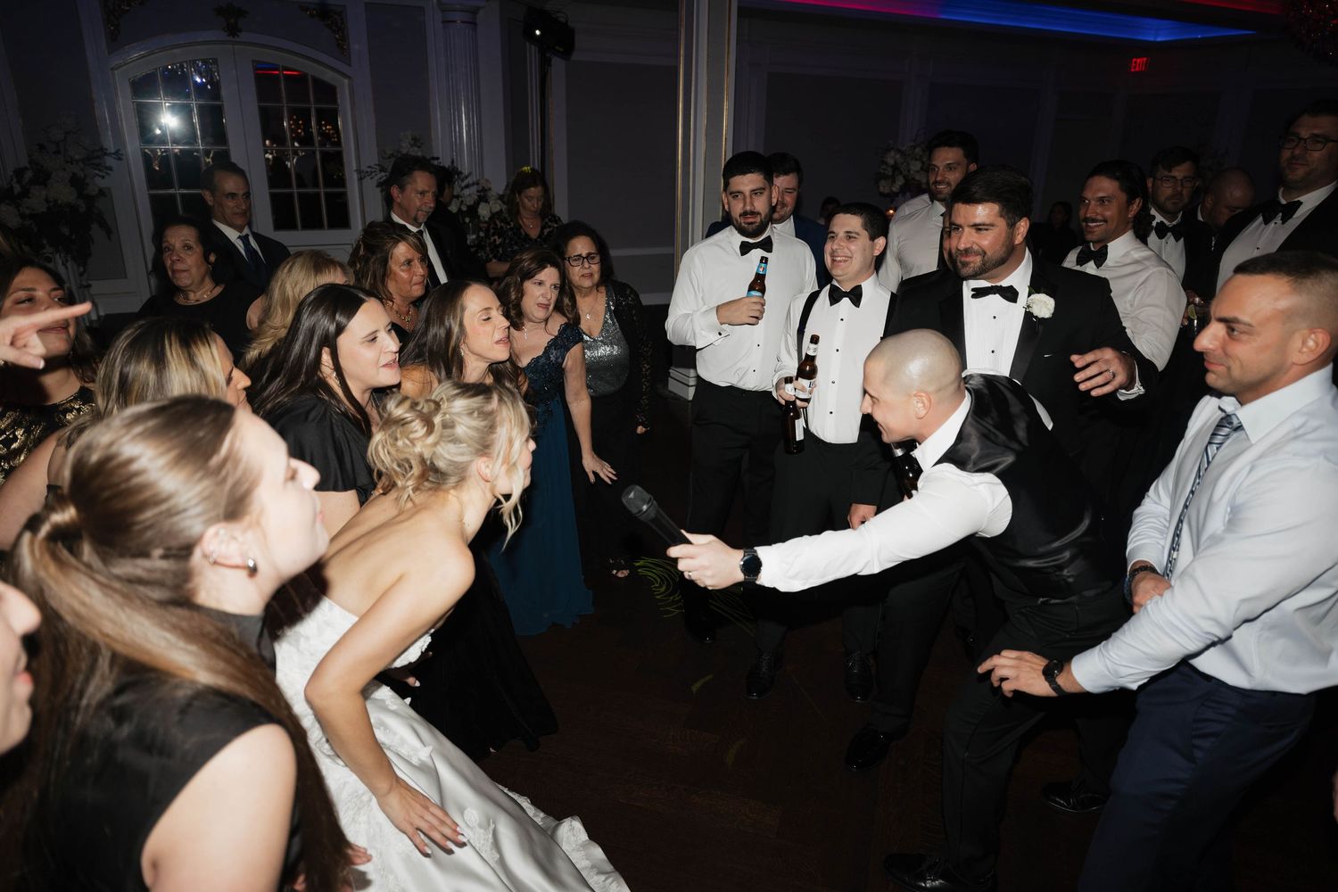 Large group of wedding guests dancing and celebrating on a dark dance floor with blue accent lighting.