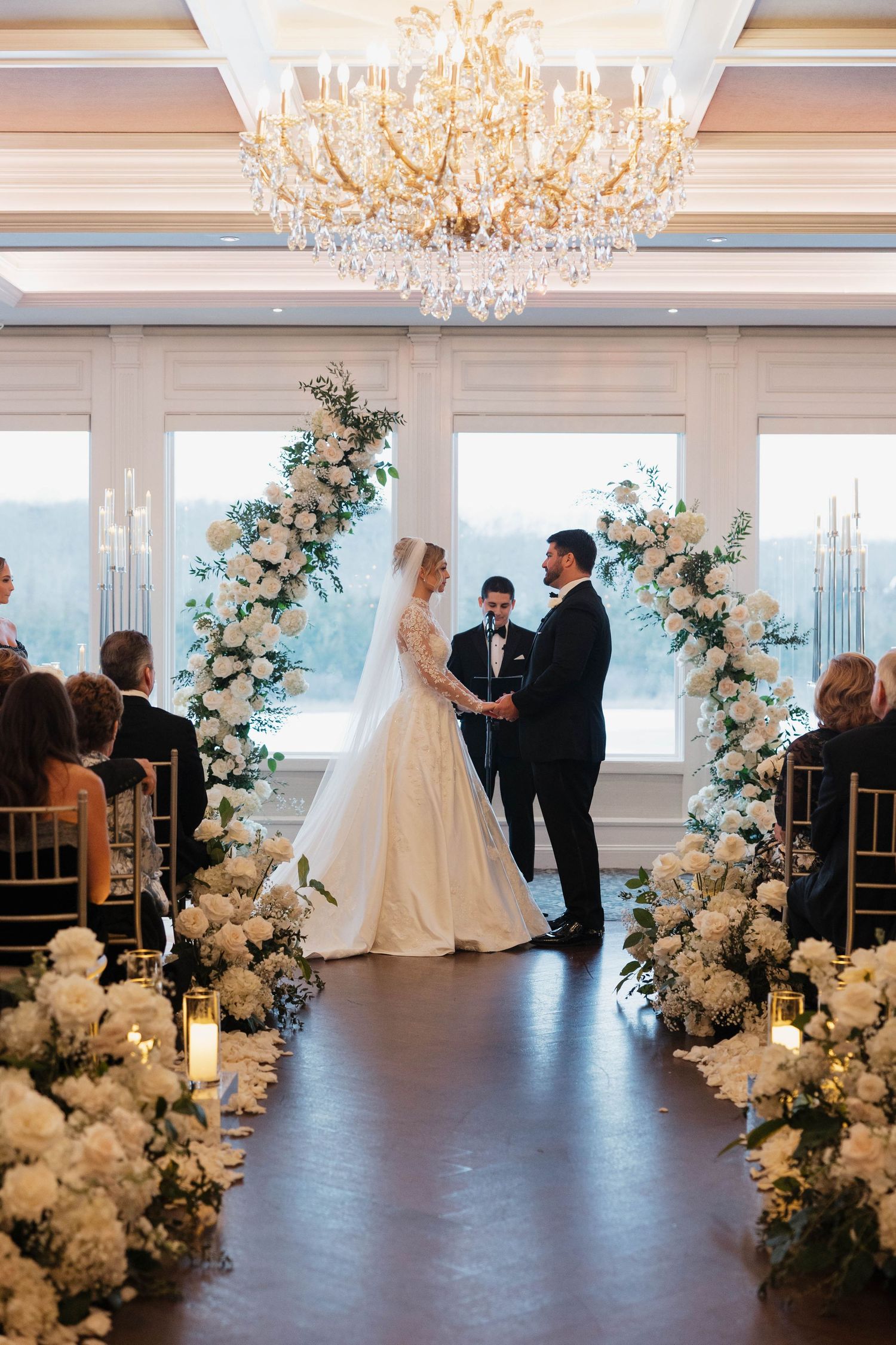 Wedding ceremony space with white floral arches and chandeliers overlooking waterfront views.