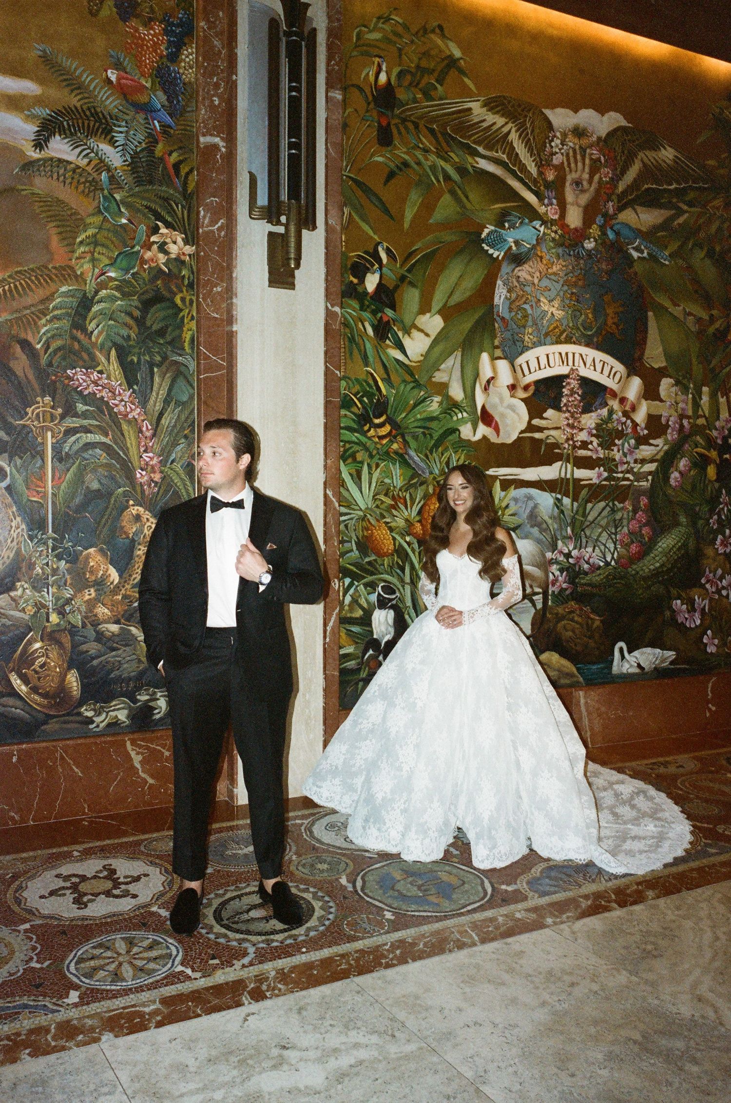 Elegant wedding photo shoot against a wall with ornate tropical murals and marble flooring.