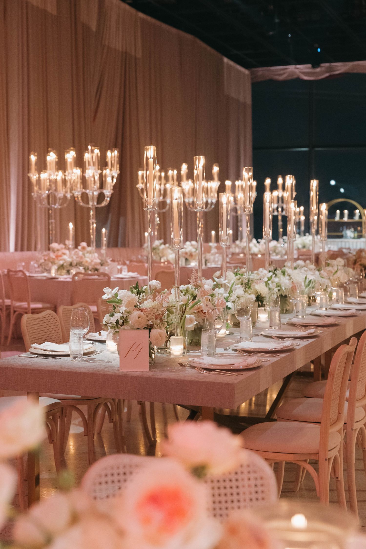 Long banquet table adorned with crystal candelabras and delicate white floral arrangements in soft pink lighting.