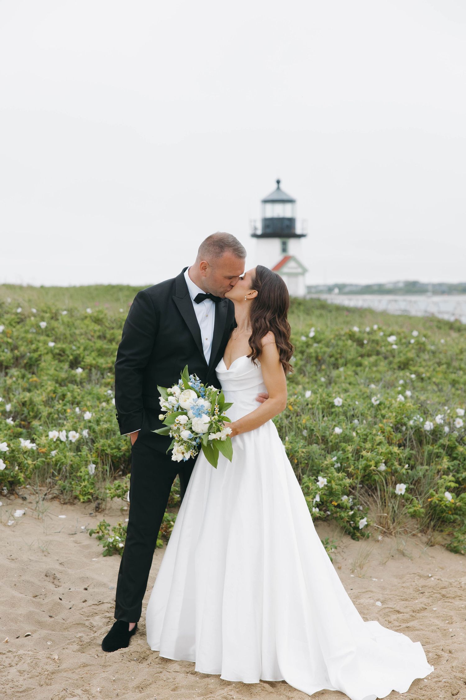 Romantic wedding couple poses in field of wildflowers by the ocean.