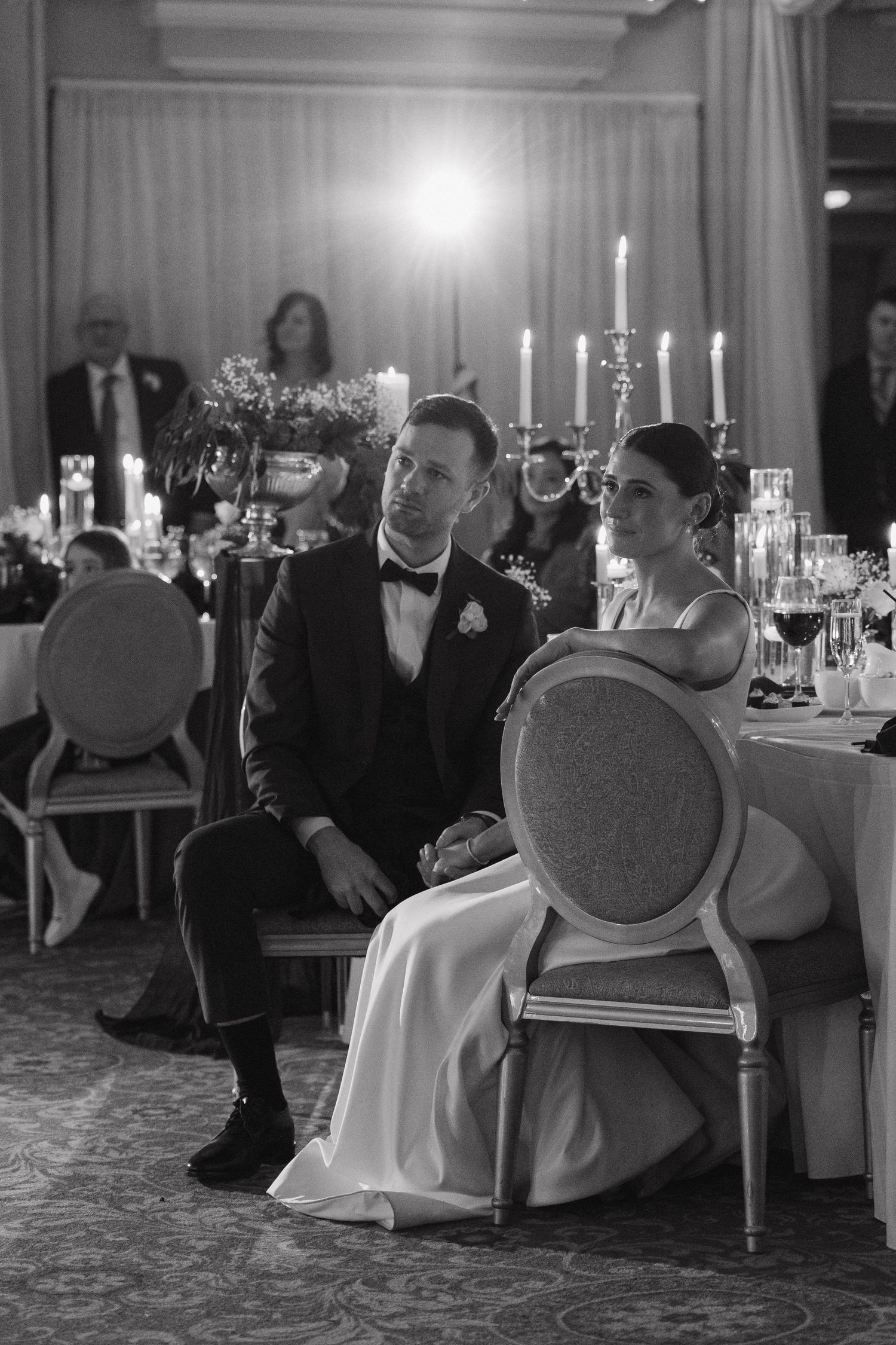 Guests enjoying a formal dinner reception in an elegant room with chandeliers and candlelight.