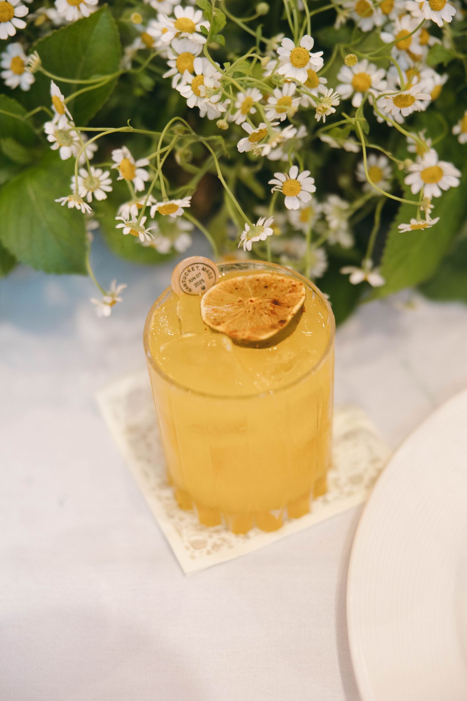 Yellow cocktail garnished with citrus and fresh daisies on white linen.