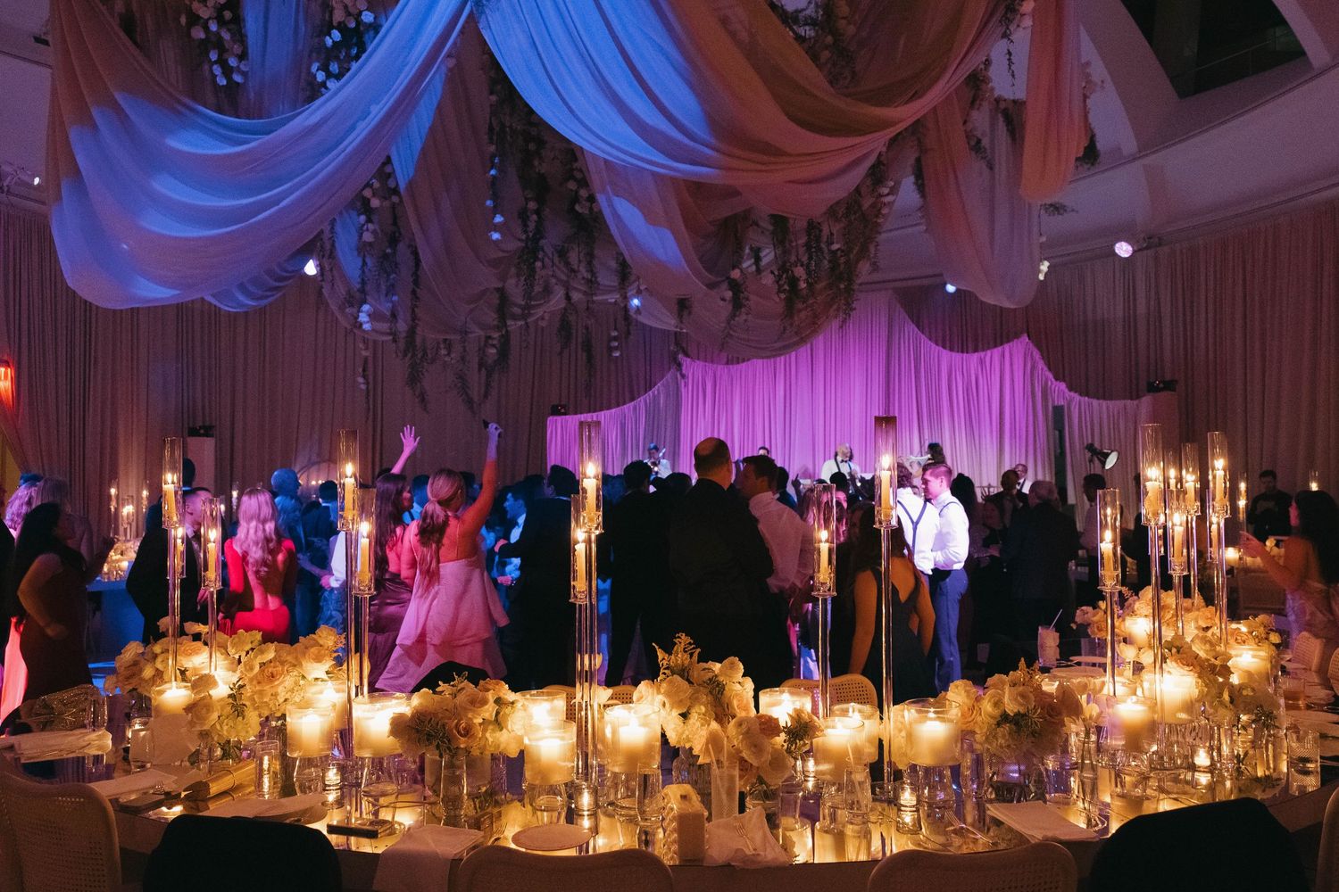 Wedding reception venue decorated with dramatic blue uplighting and elegant white draping.
