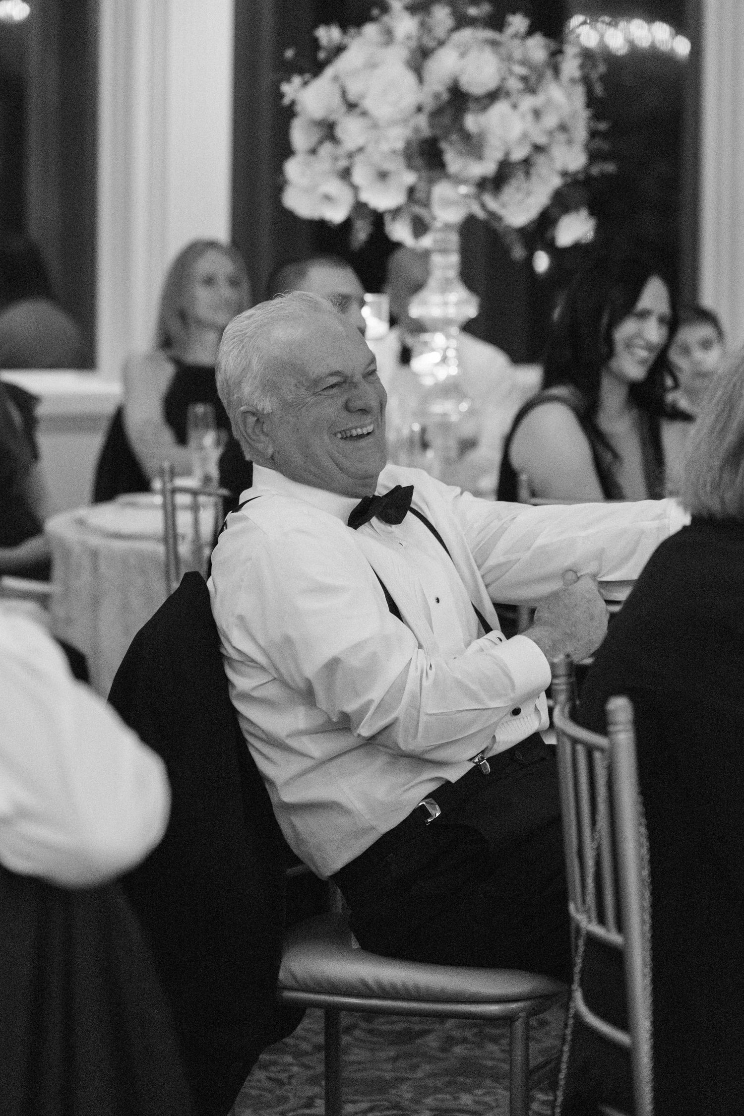Wedding guest in formal attire laughing during reception festivities.