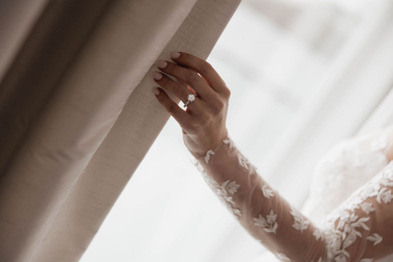 Artistic close-up of delicate lace details on wedding dress sleeve in soft light.