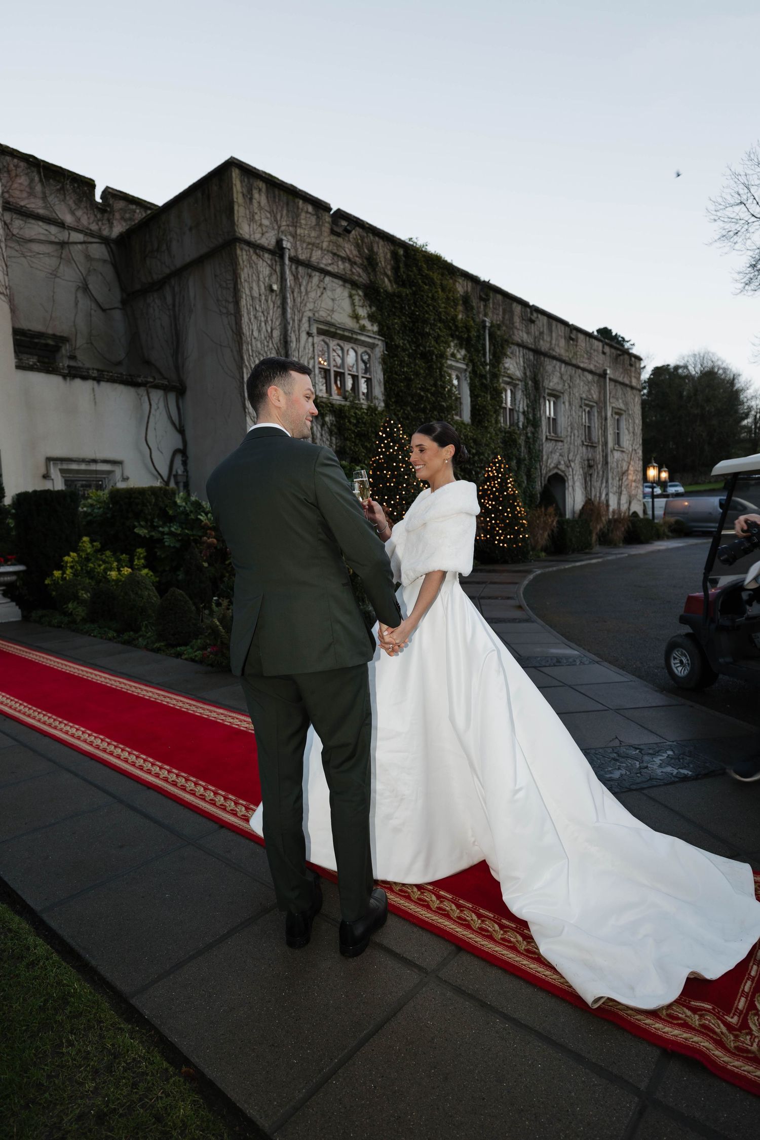 Wedding couple poses on red carpet outside elegant stone building entrance.