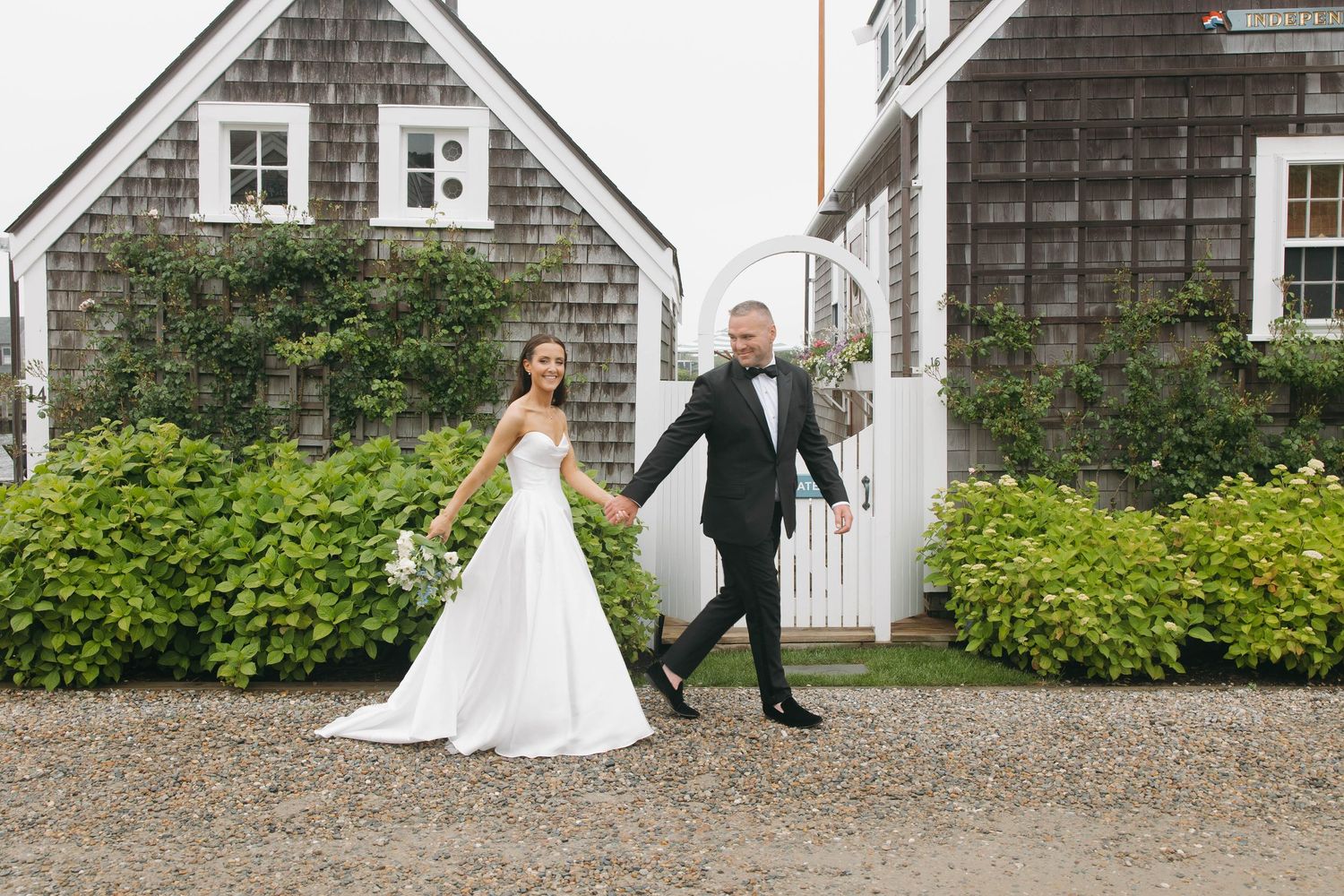 Wedding couple poses by antique car outside historic shingle style buildings.
