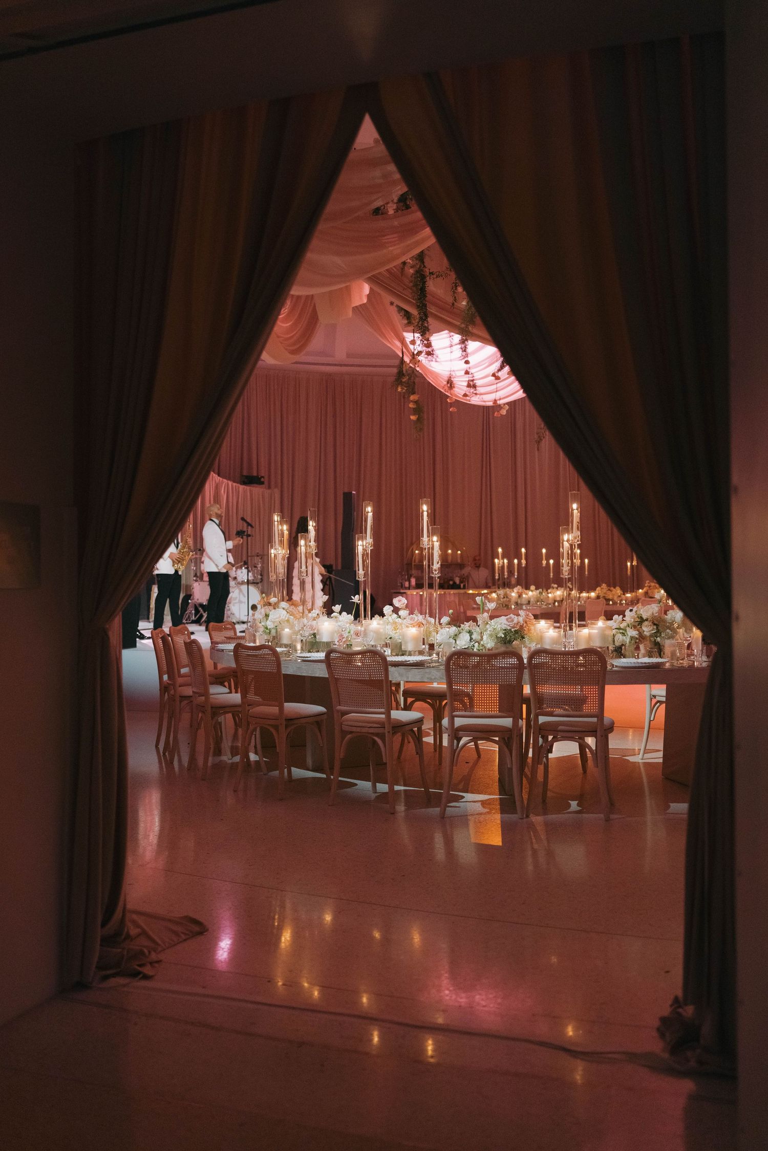 View through draped curtains of an elegantly decorated reception hall with crystal chandeliers.