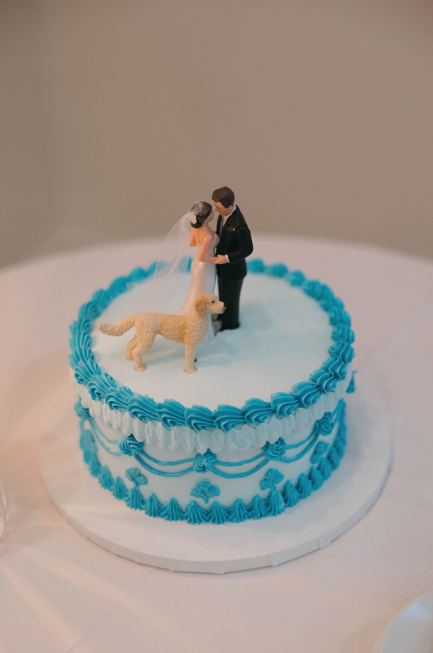 Small wedding cake with blue frosting details and miniature couple cake topper.