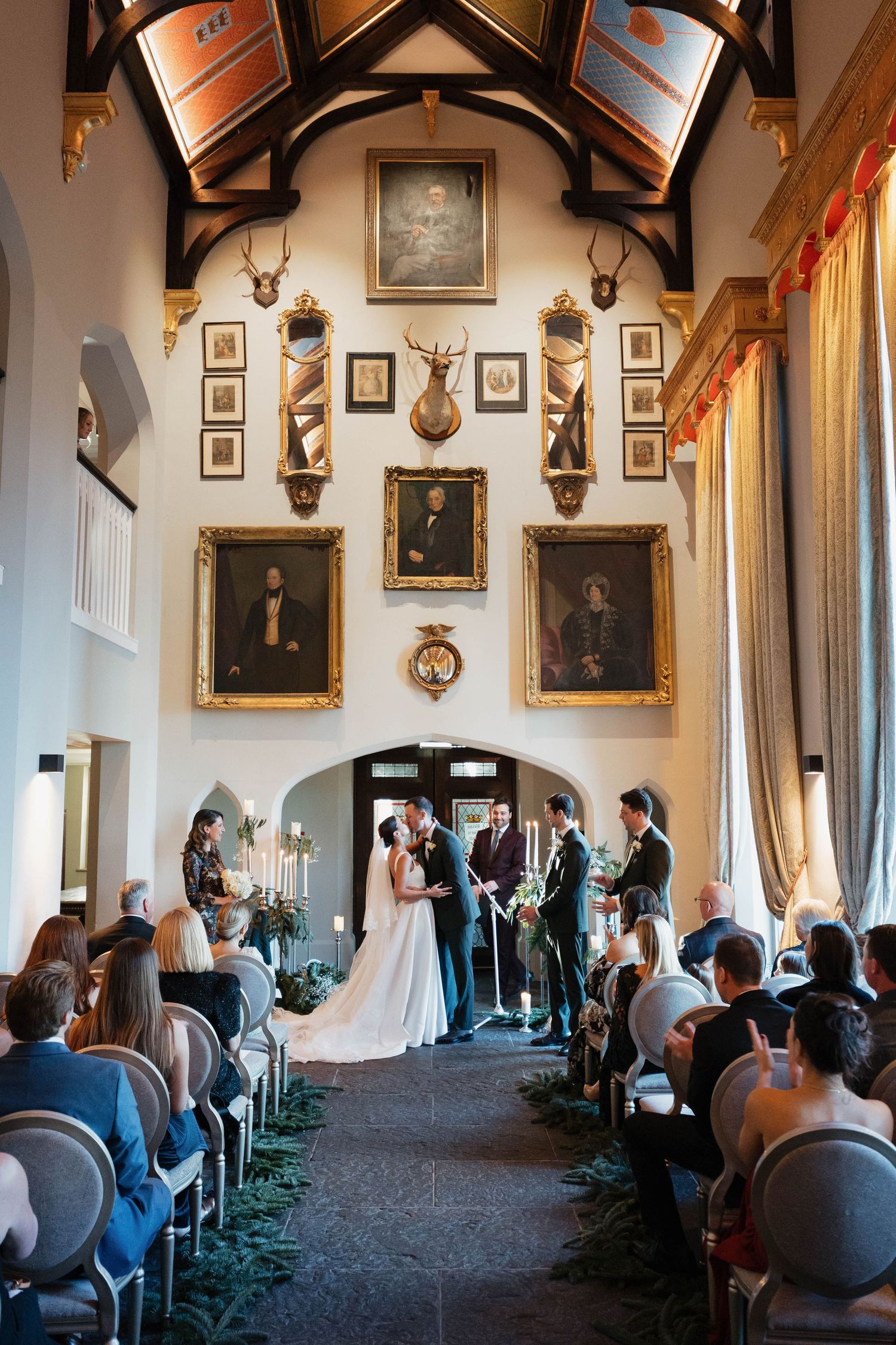 A grand hall with arched ceilings and portrait-lined walls filled with wedding guests.