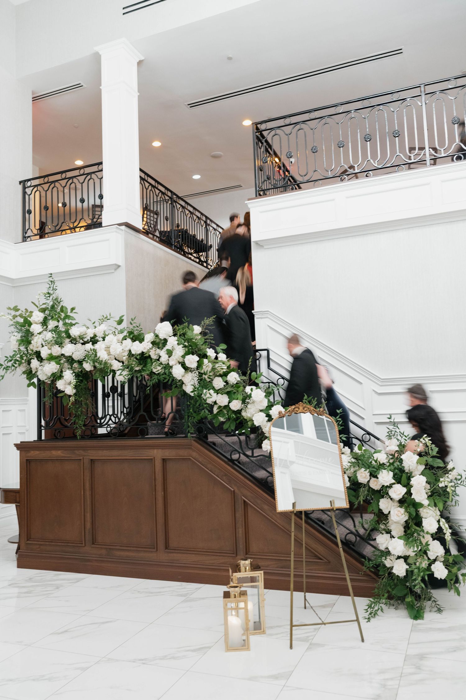 Grand staircase decorated with white floral arrangements and lanterns at an elegant venue.