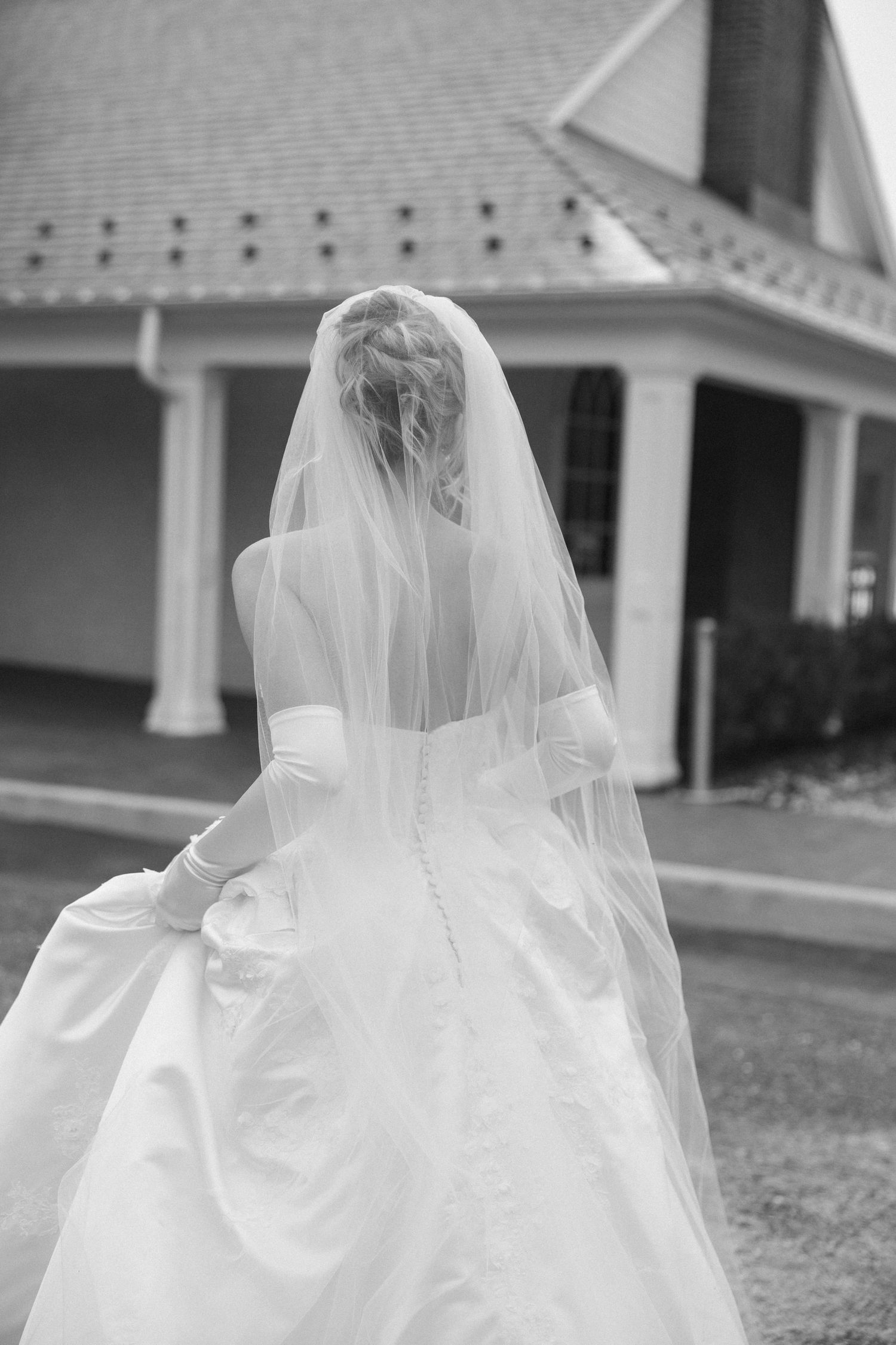 The back details of a white wedding gown and veil are captured in black and white photography.