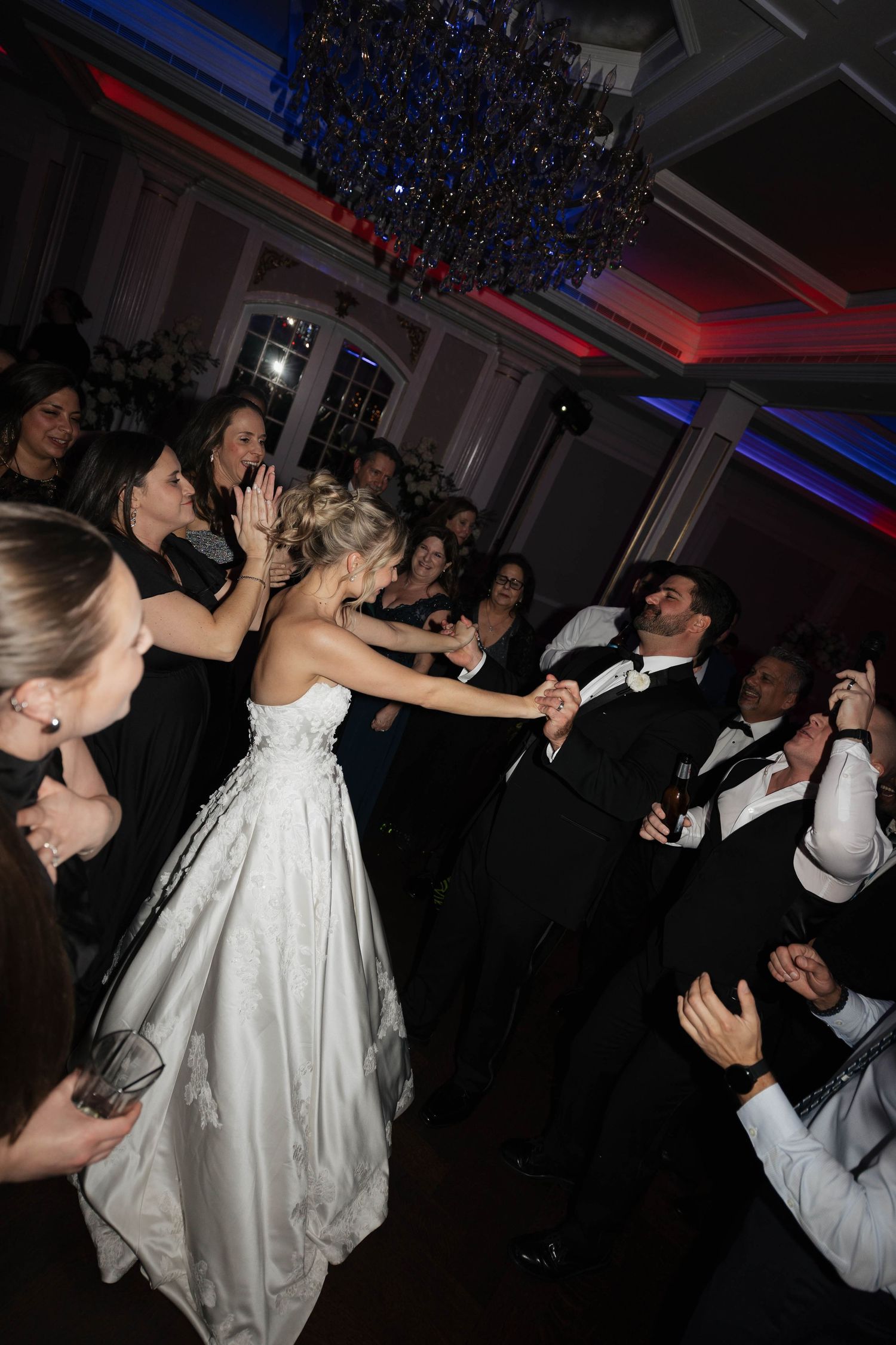 Wedding party members dance together during reception celebration under colored lights.