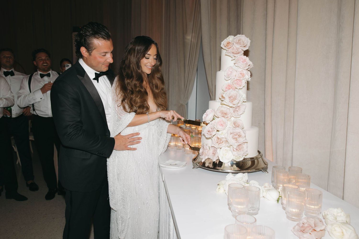 Elegant white wedding cake display with draped fabric backdrop at reception venue.