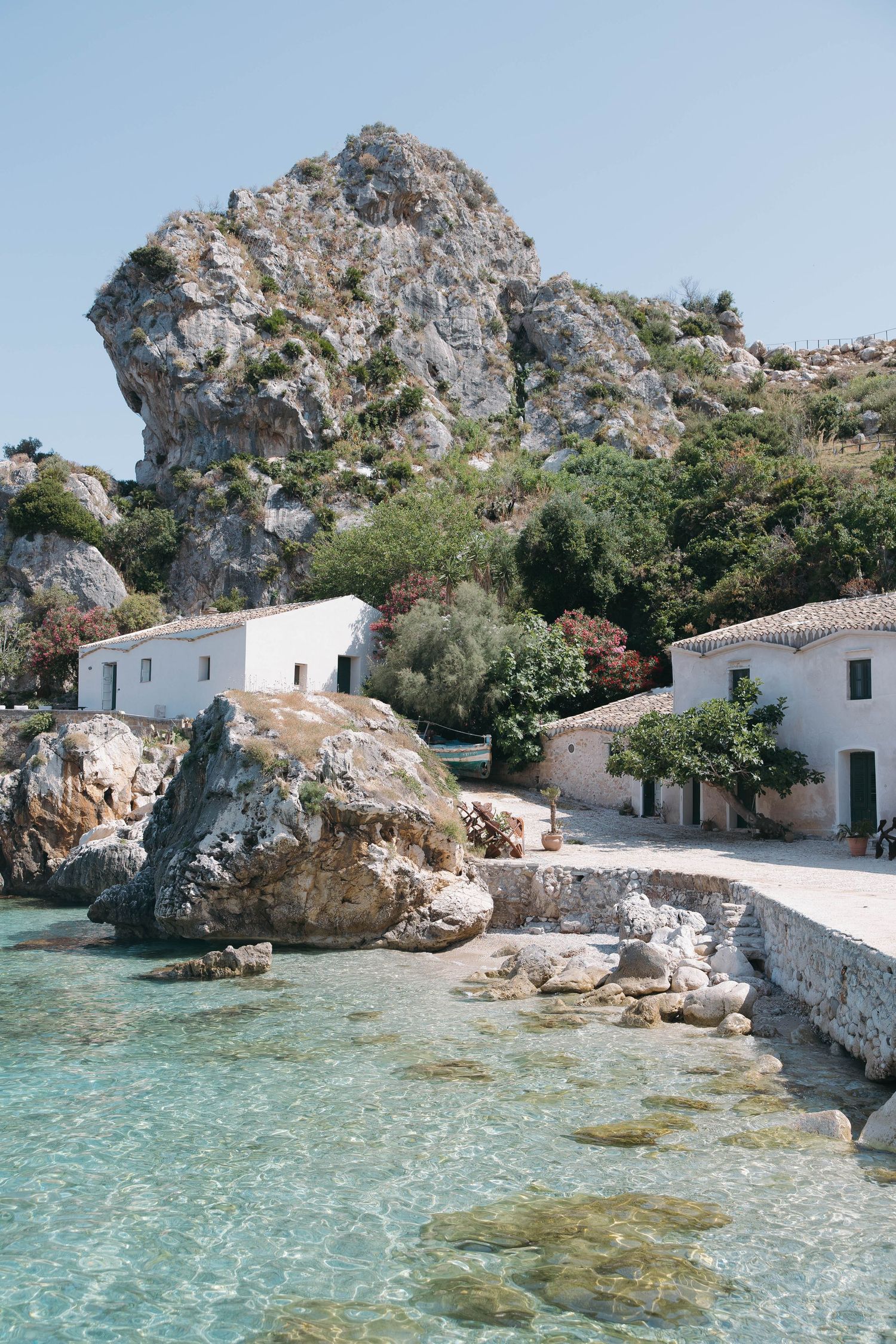 White coastal houses nestled among rocky cliffs overlooking crystal clear turquoise Mediterranean waters.