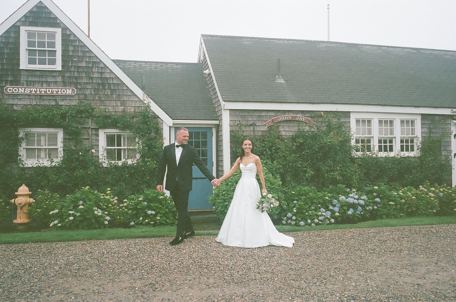 A rustic green-roofed farmhouse with white trim and blooming gardens serves as a charming wedding venue backdrop.