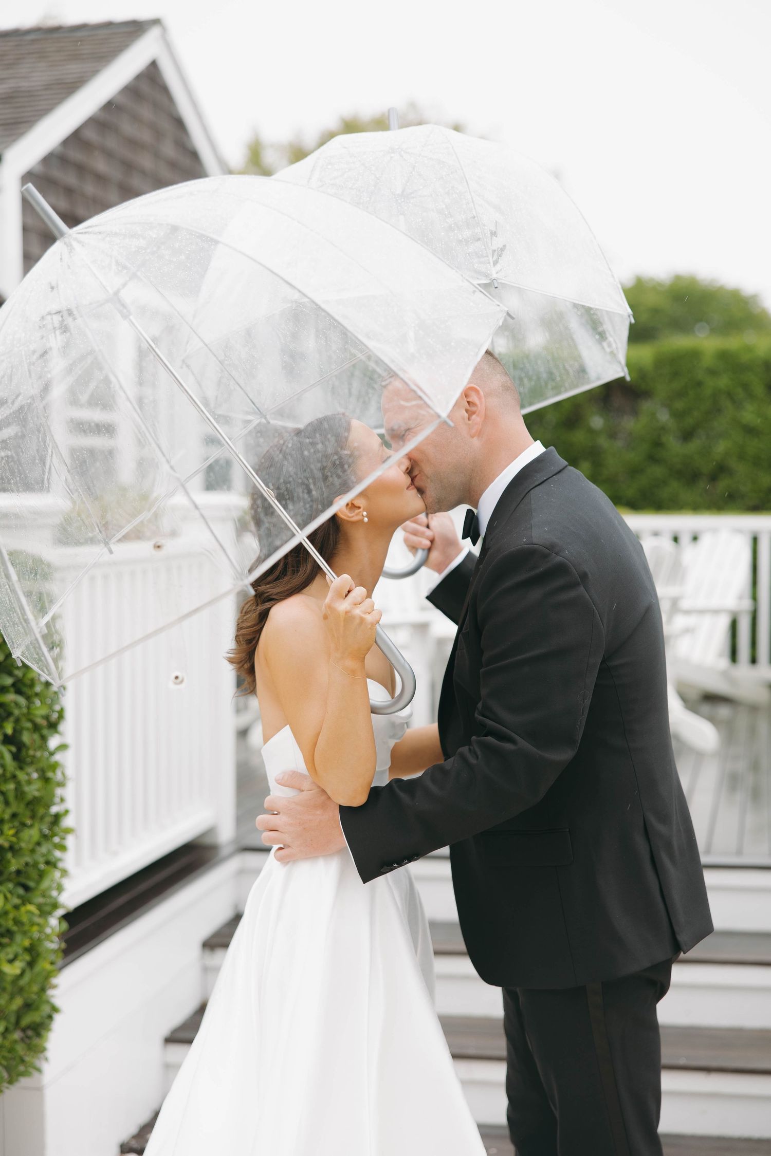 Couple shares romantic moment under clear umbrellas on rainy wedding day.