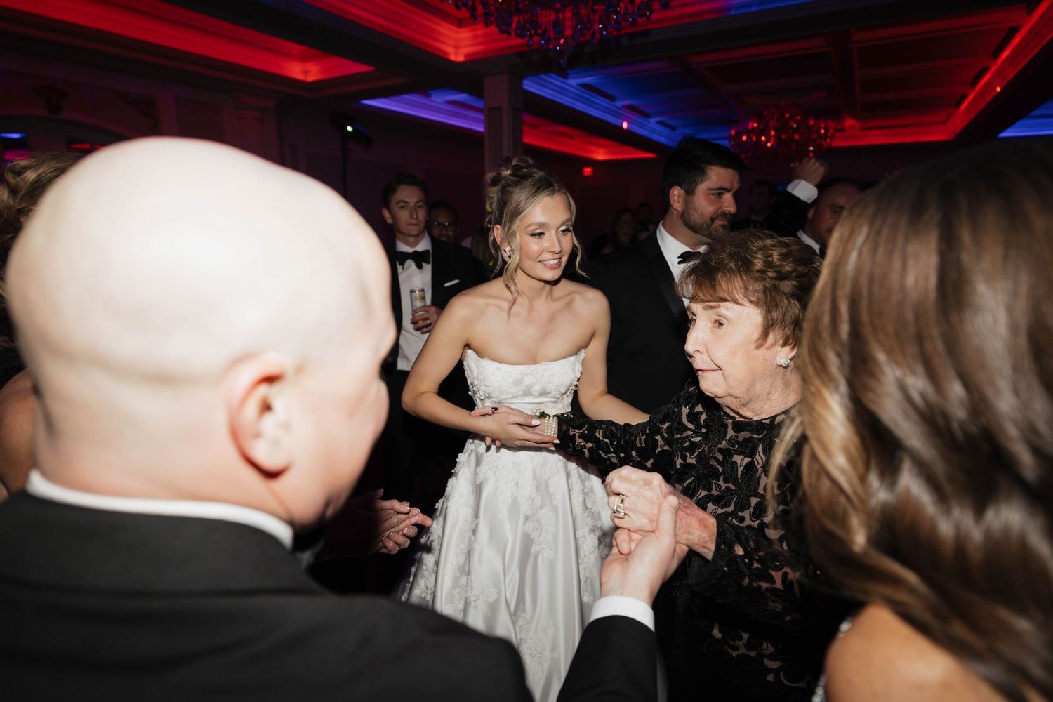 Guests dancing and celebrating at wedding reception under red ambient lighting.