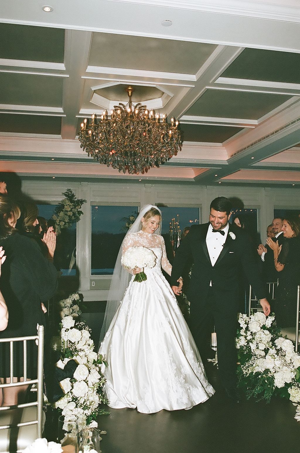 Elegant wedding reception scene with couples dancing under a crystal chandelier in a formal ballroom setting.