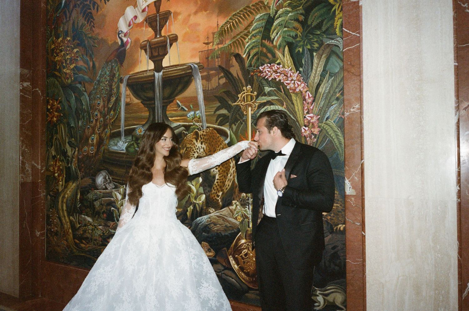Couple posing for wedding photos against an ornate wall mural with golden tones.