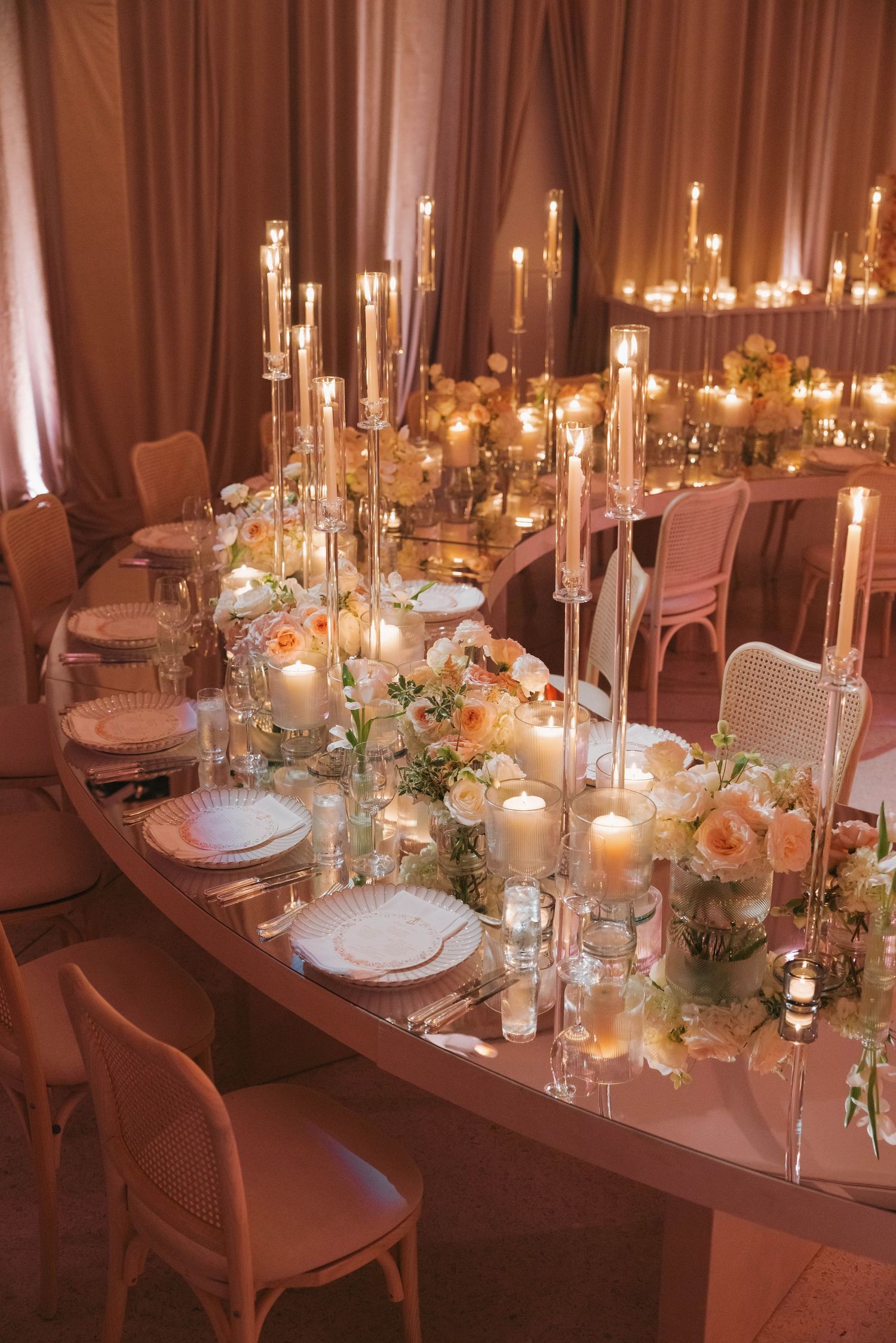 Intimate table setting with tall glass candlesticks, white place settings, and peach floral arrangements.