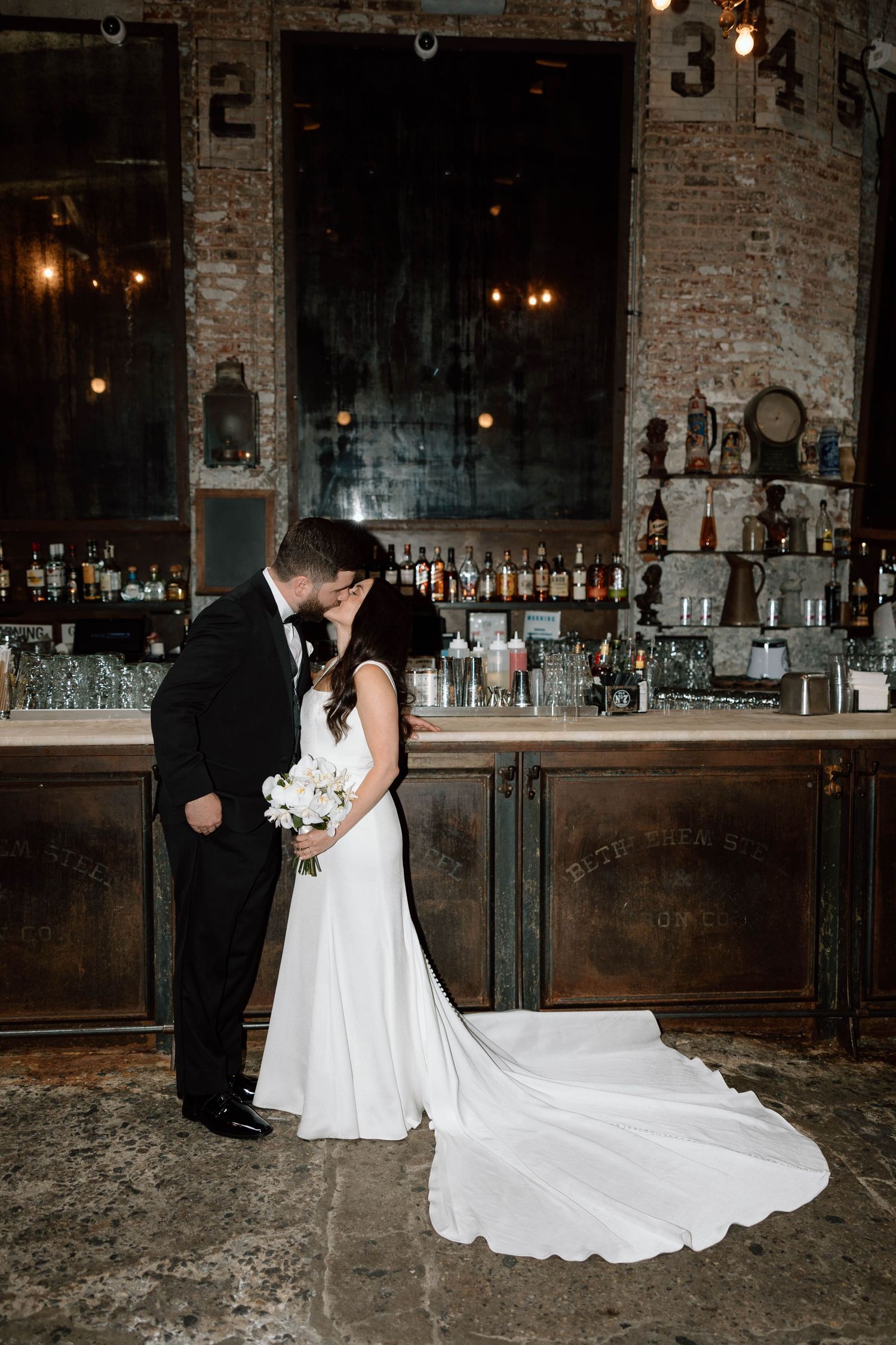 Wedding couple shares intimate moments in a rustic bar setting with exposed brick walls.