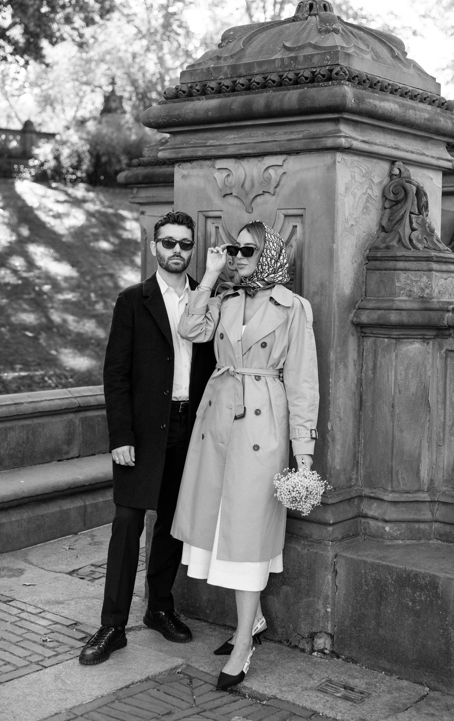 A couple in formal attire poses for wedding photos against stone architecture in black and white.