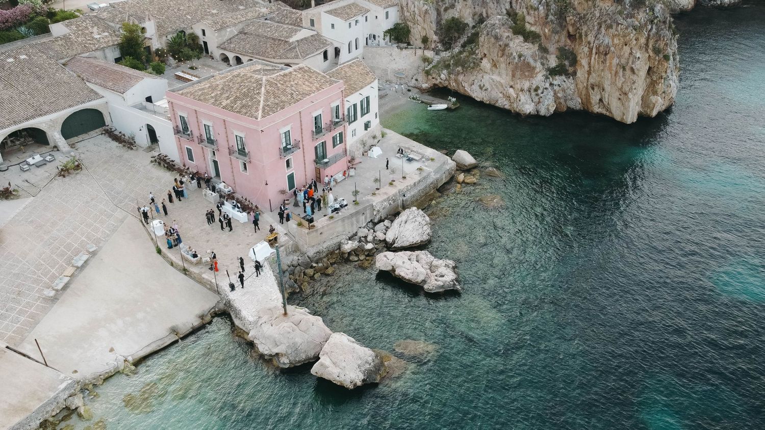 Aerial view of seaside architecture and rocky outcrops meeting turquoise Mediterranean waters.