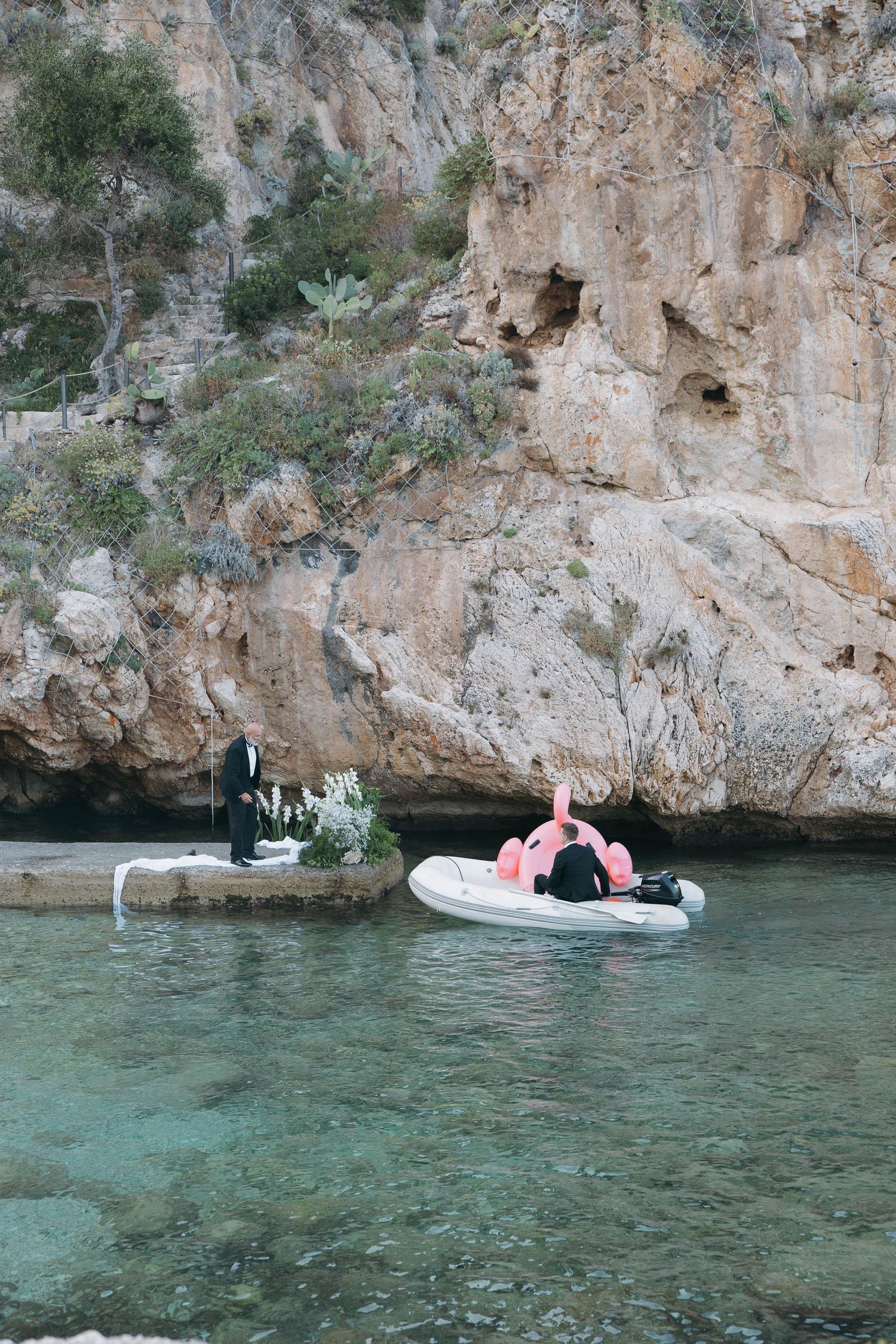 Inflatable pink flamingo float bobs in turquoise waters near limestone cliffs.
