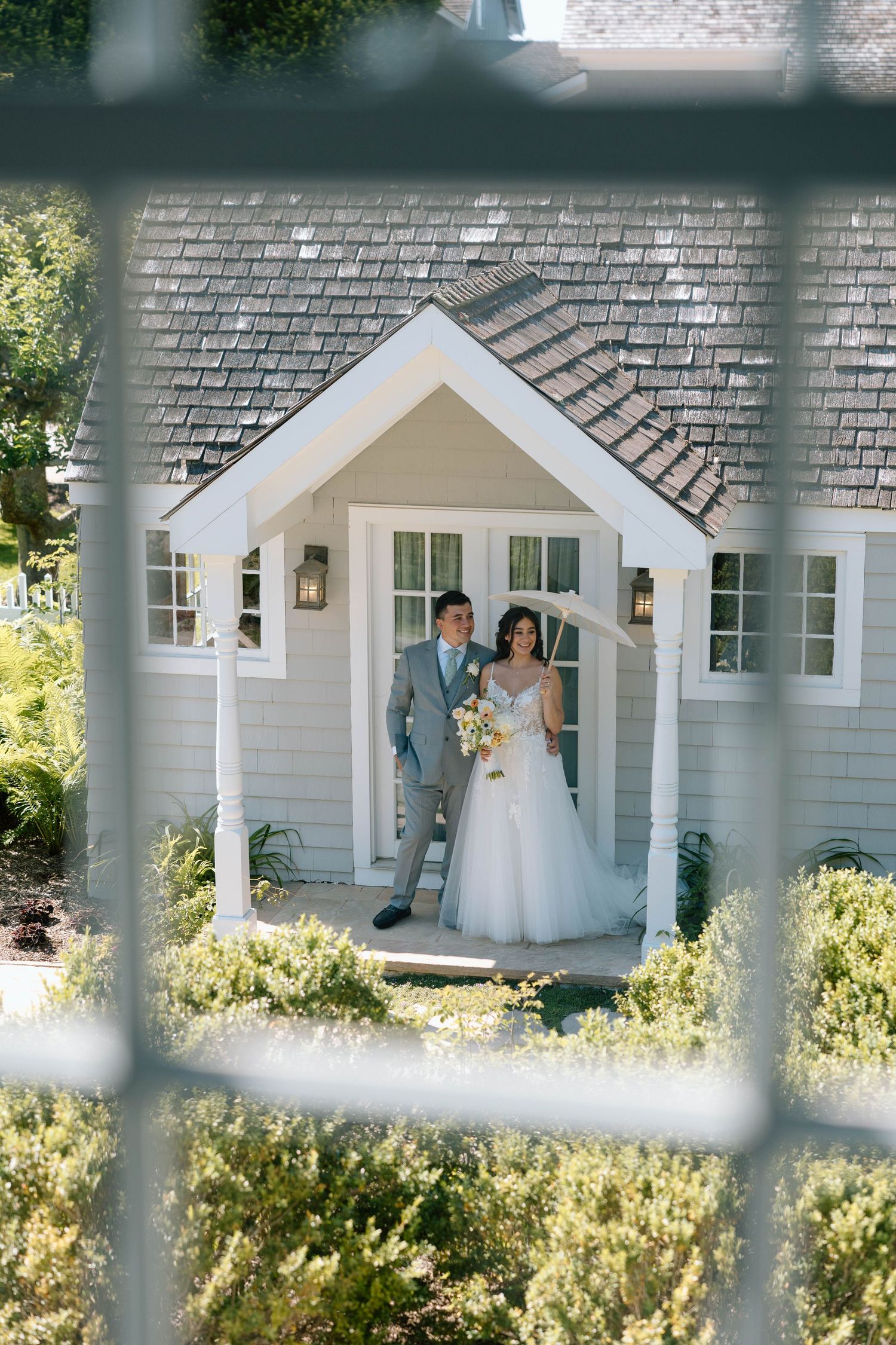 Wedding couple framed in white cottage doorway surrounded by lush garden.