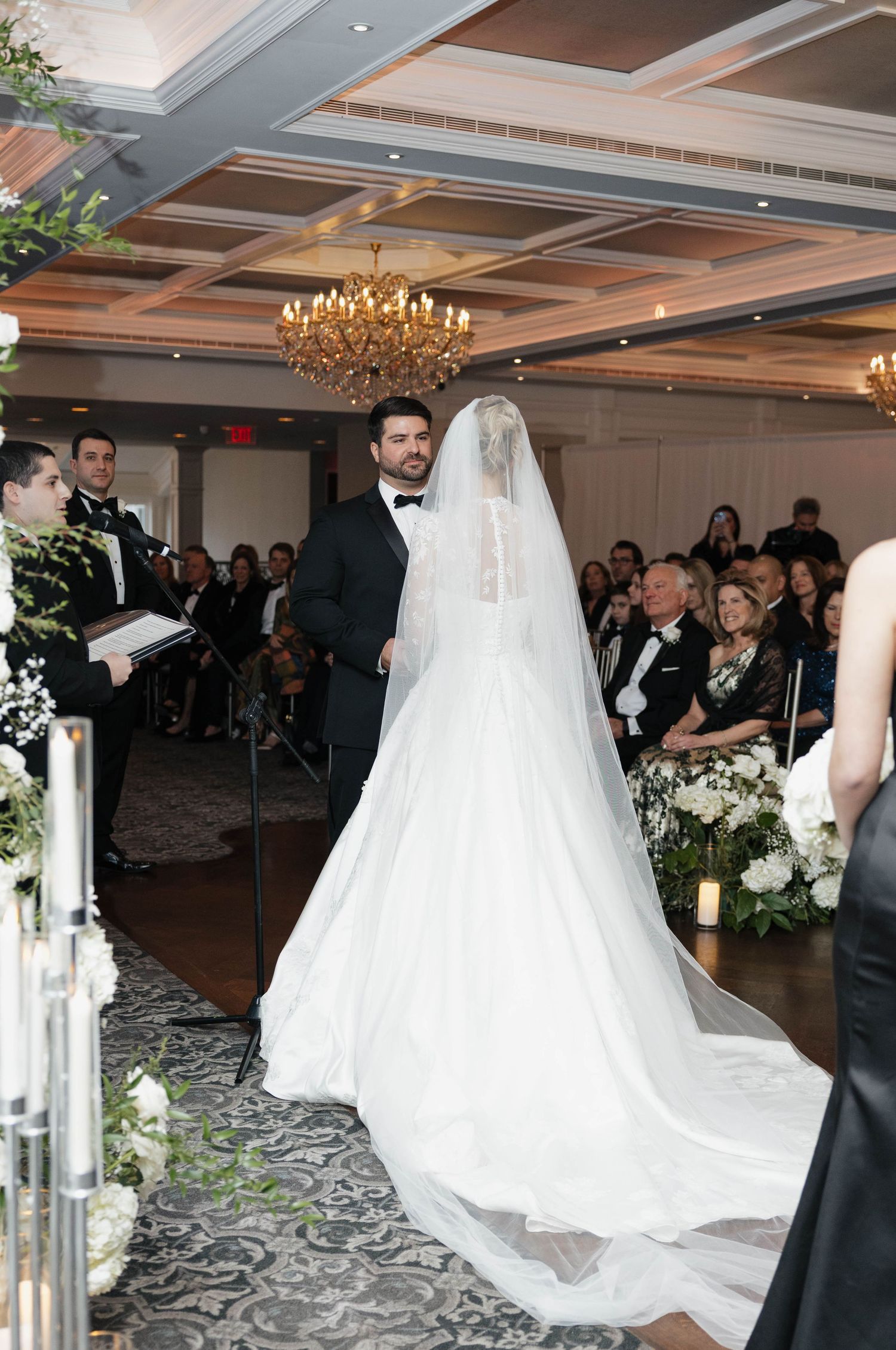 Wedding ceremony in elegant ballroom with coffered ceiling and floral decorations.