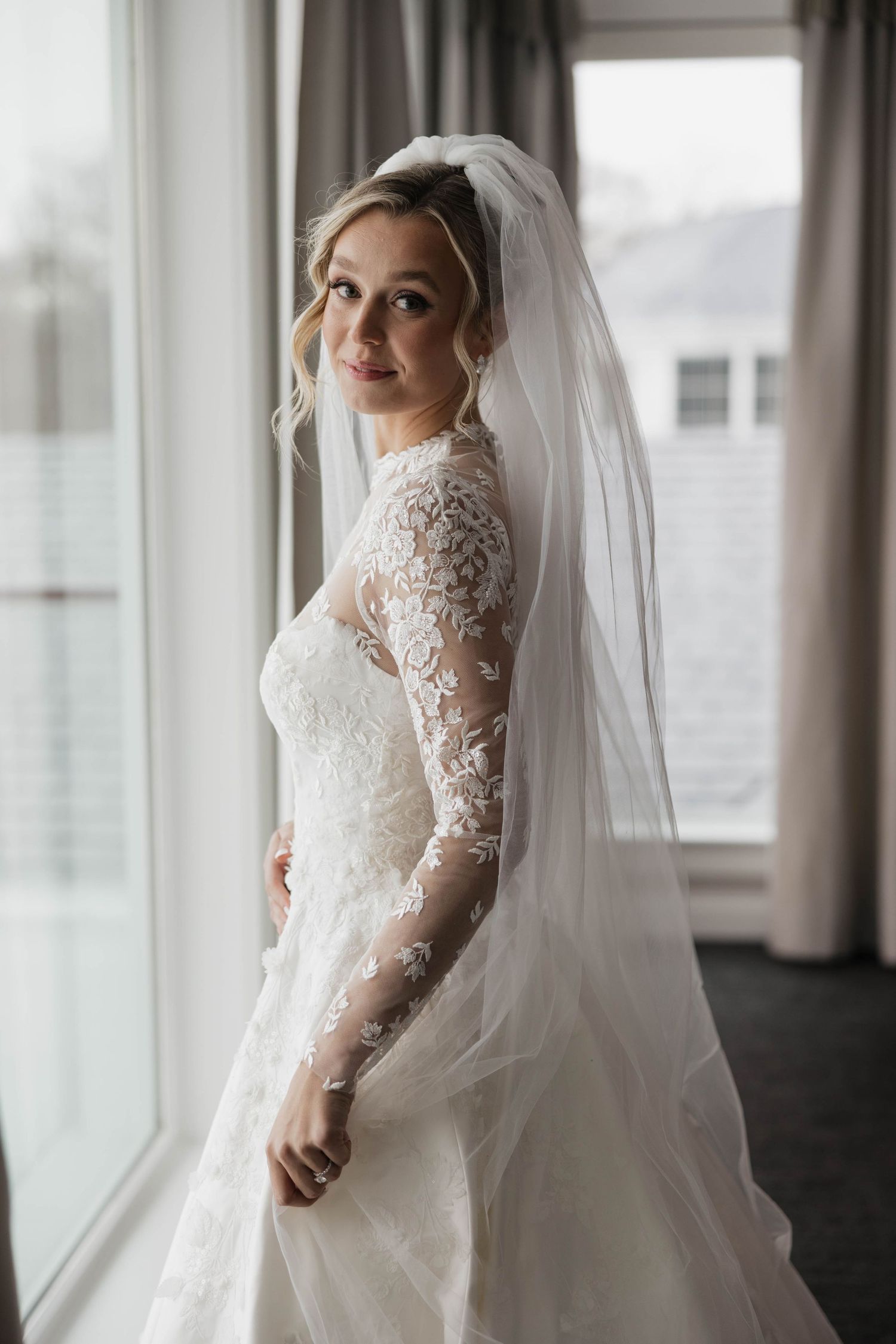 Elegant bridal portraits by large windows showing intricate lace sleeve details.