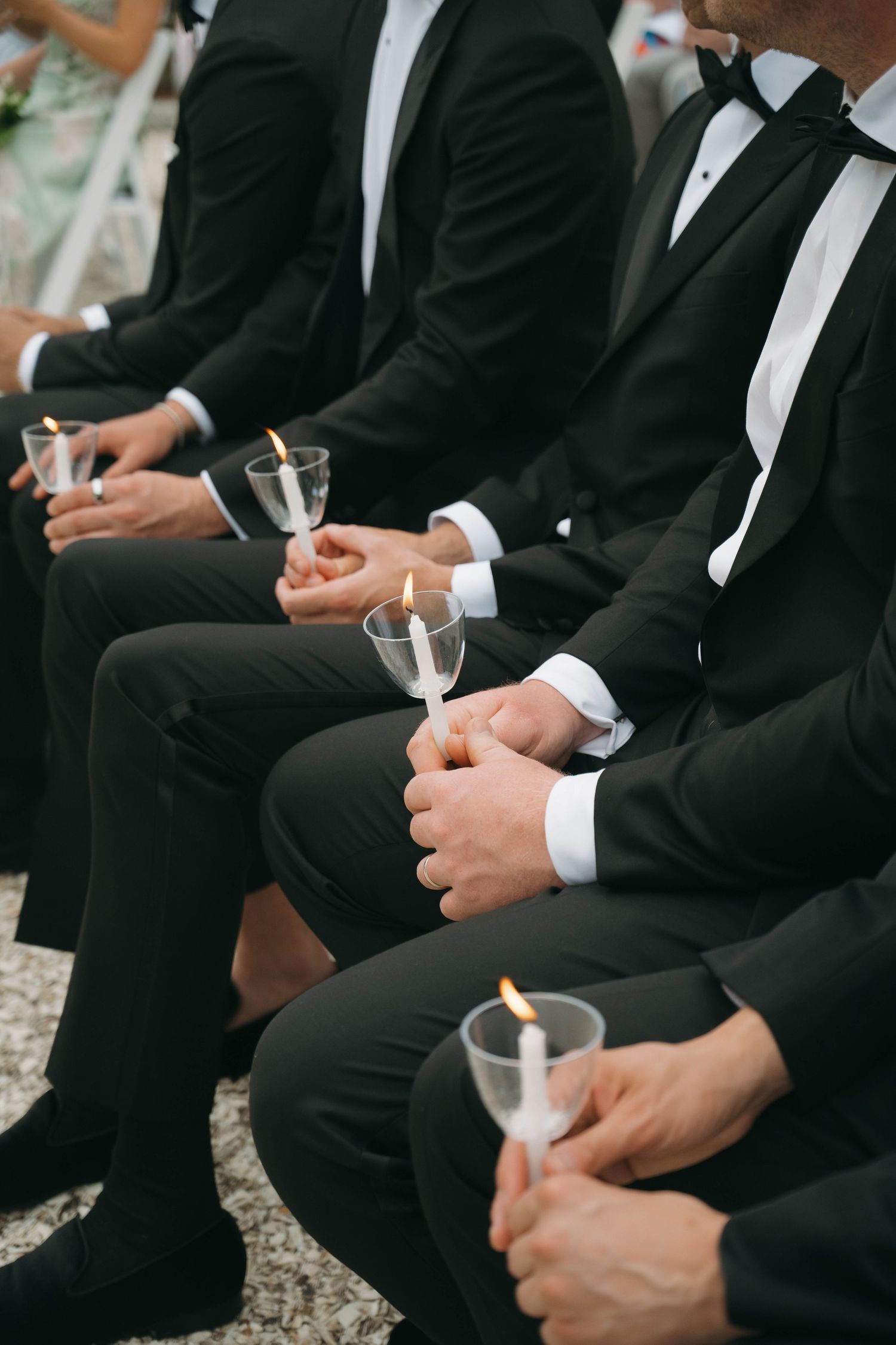 Close-up of groomsmen in black tuxedos holding glasses during wedding ceremony.