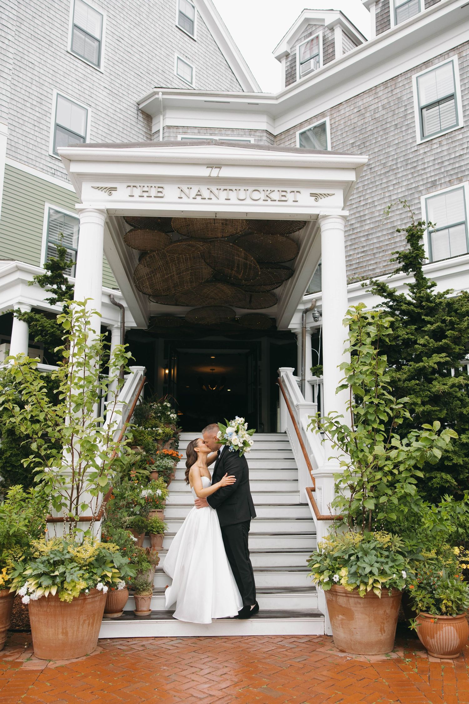 Couple shares romantic moment outside The Nantucket Hotel entrance surrounded by potted plants.
