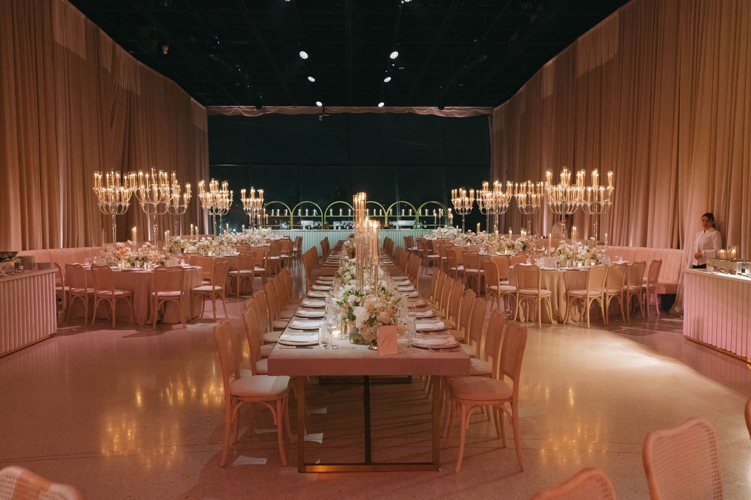 Wide view of an elegant wedding reception space with rows of tables and warm ambient lighting.