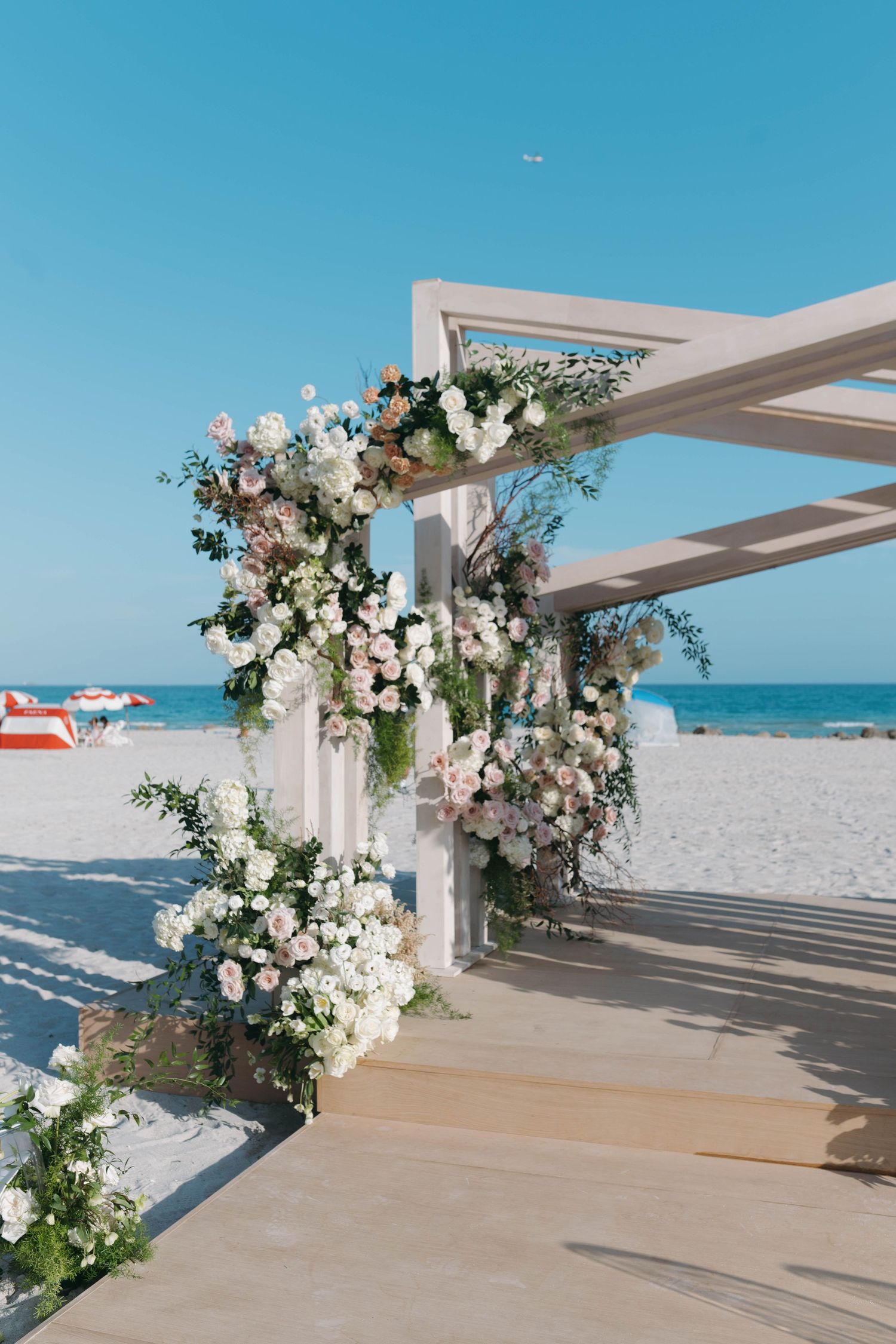 Modern beach wedding ceremony setup with white floral arrangements and ocean backdrop.