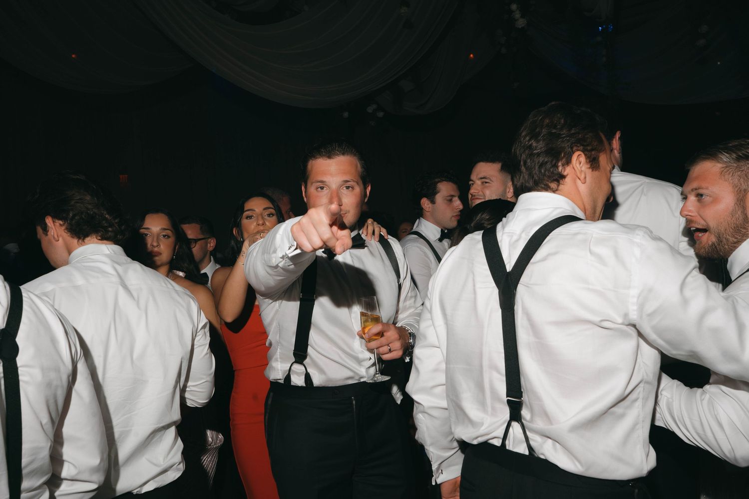Groomsmen in white shirts and suspenders celebrating on the dance floor.