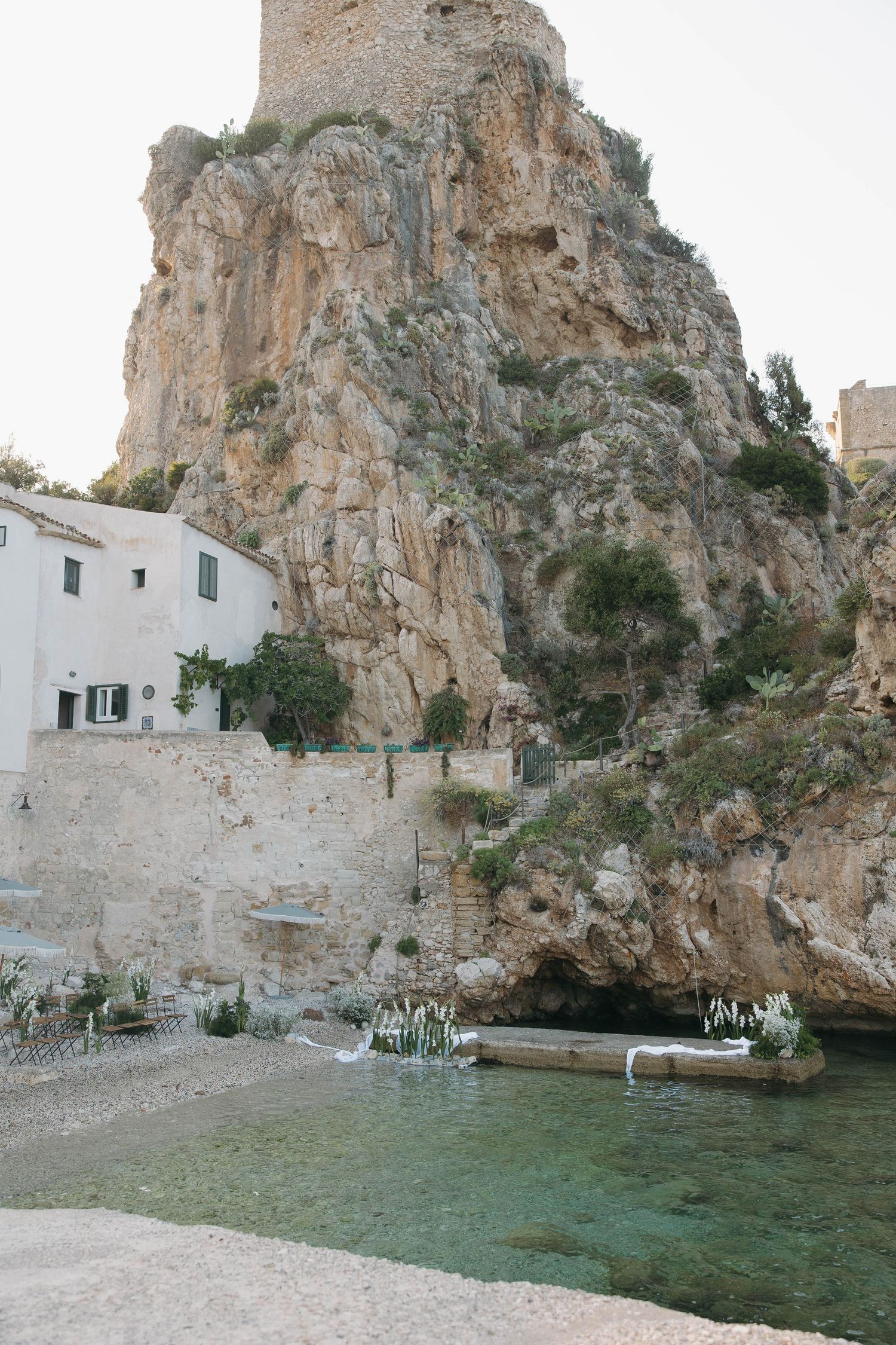 White coastal buildings integrated into dramatic limestone cliffs above clear turquoise waters.