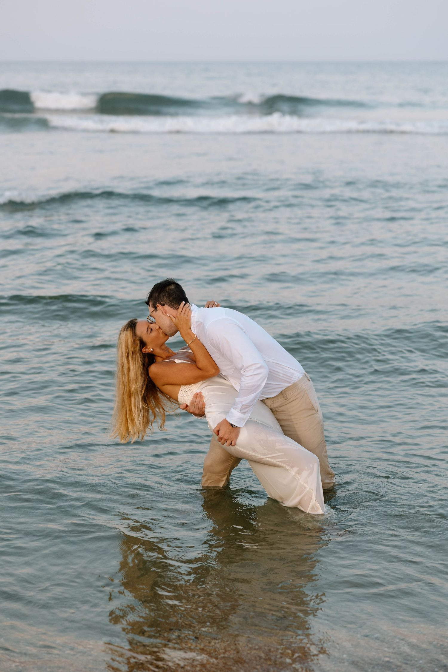 A romantic dance dip pose in the ocean waves at sunset.