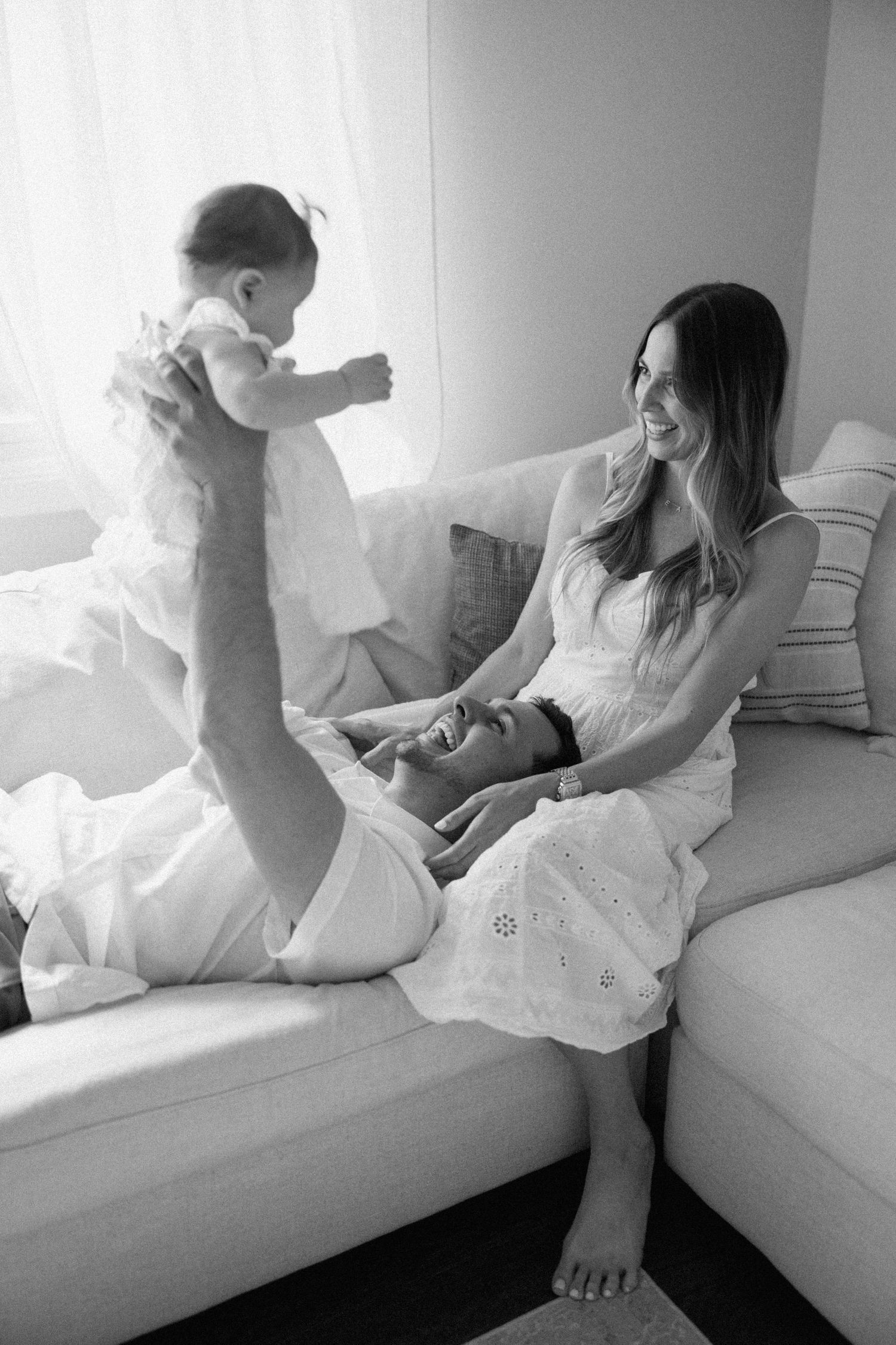 Black and white series of images showing a child in white dress playing and jumping on a couch.