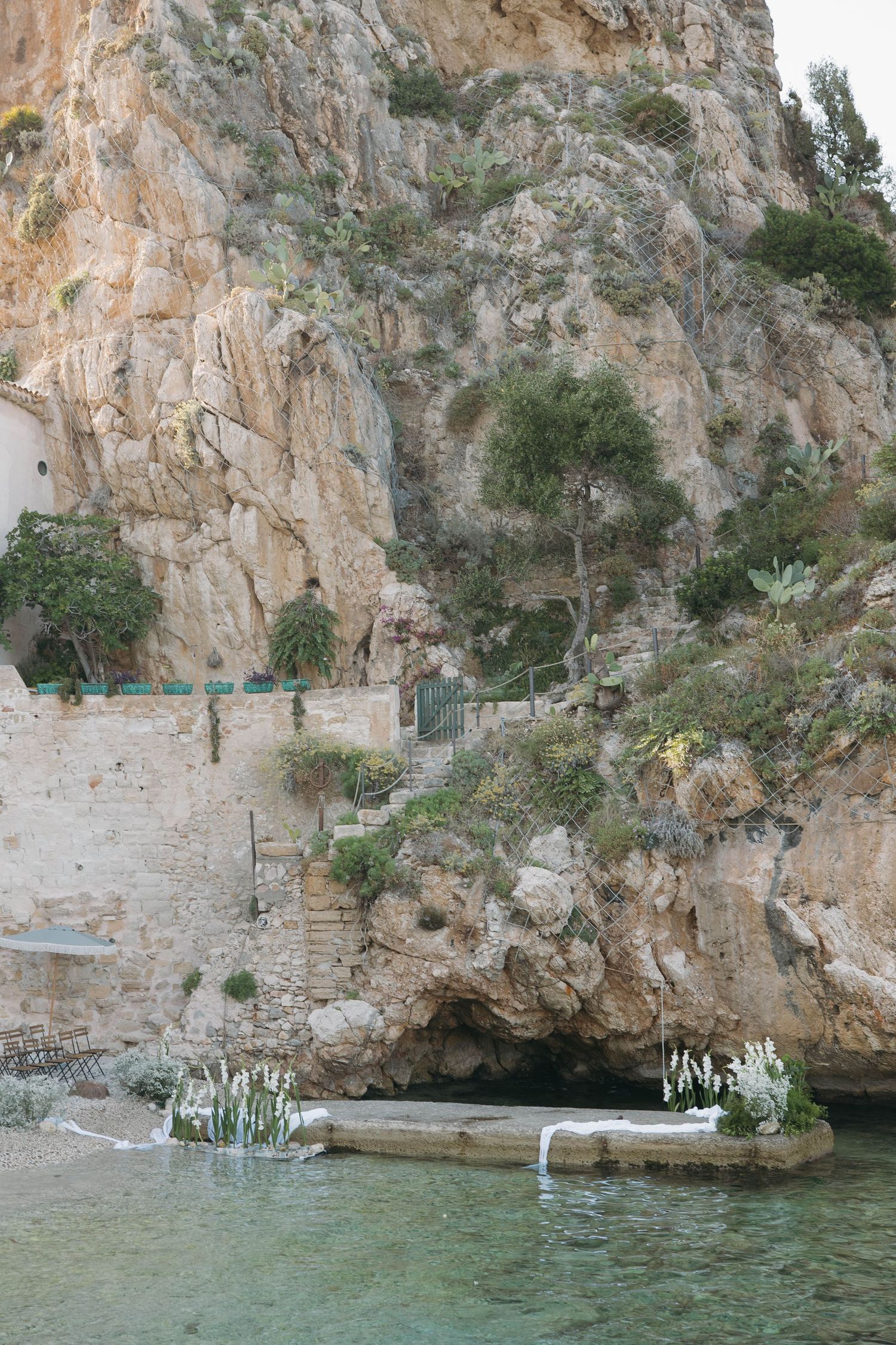 Rocky coastal cove with white stone buildings and crystal clear turquoise waters.