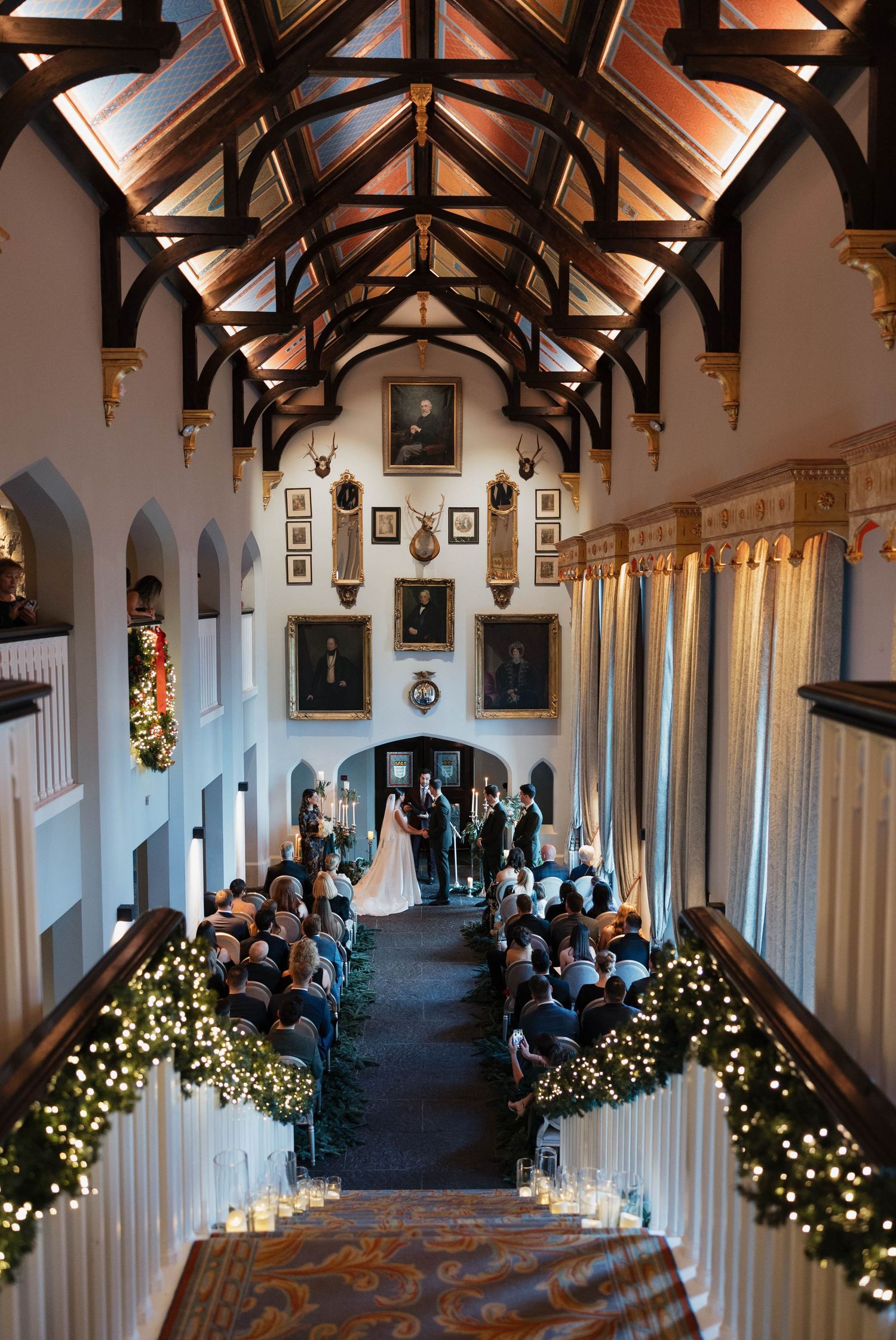 Elegant hall decorated for wedding ceremony with twinkling lights and Christmas decor along the aisle.