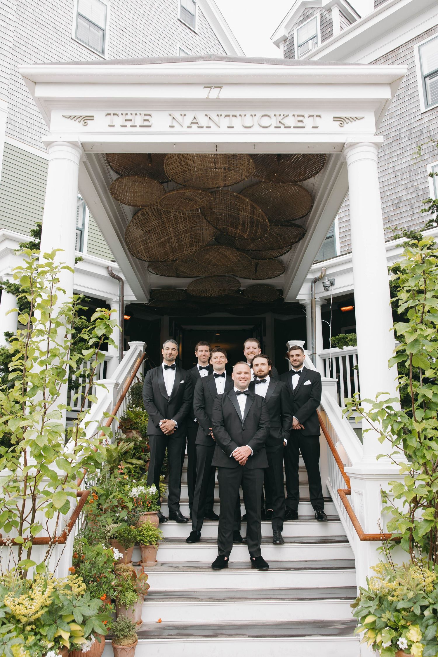 Groomsmen in black tuxedos pose on white porch steps of The Nantucket Hotel.
