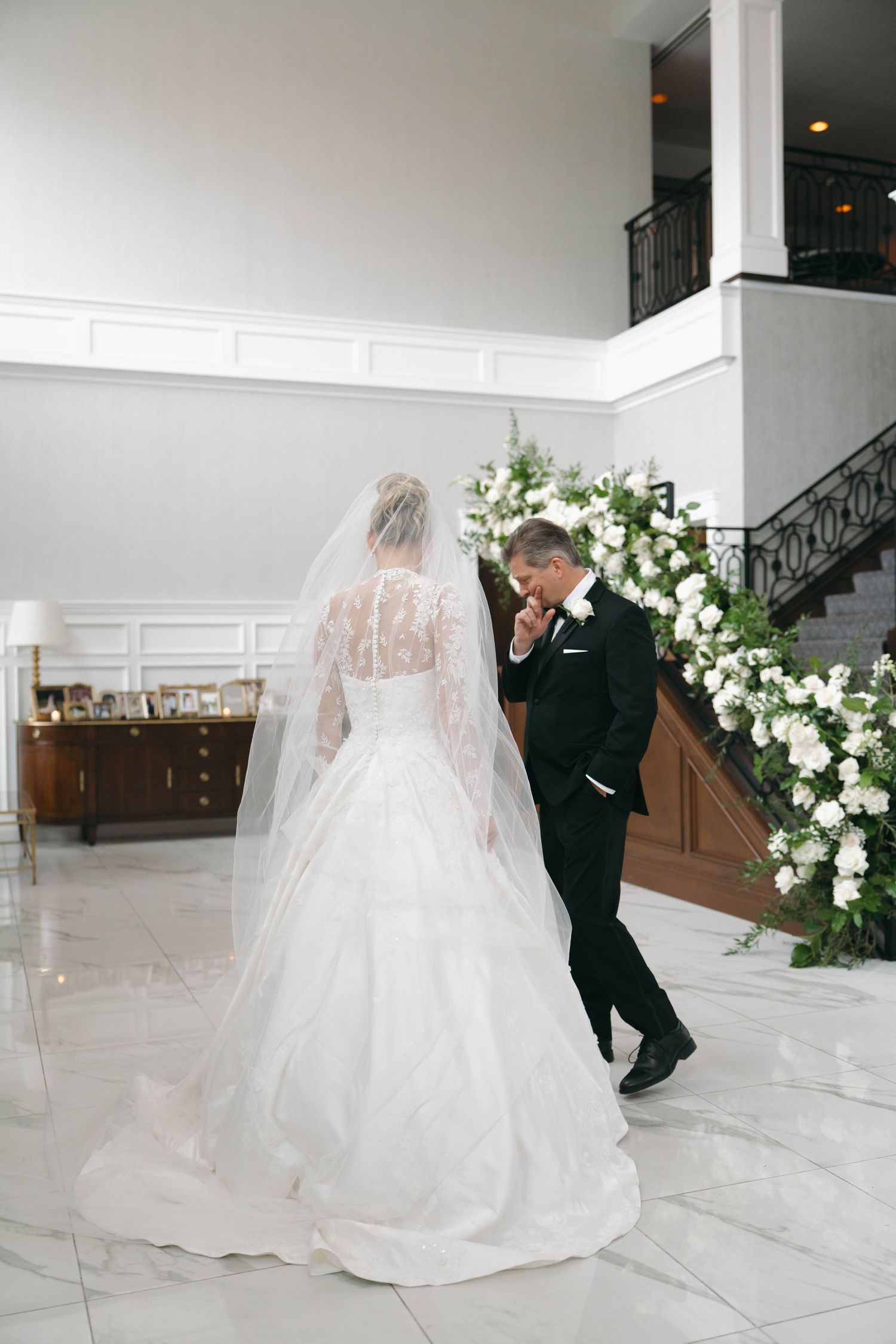 A wedding couple in formal attire standing in an elegant white marble foyer.