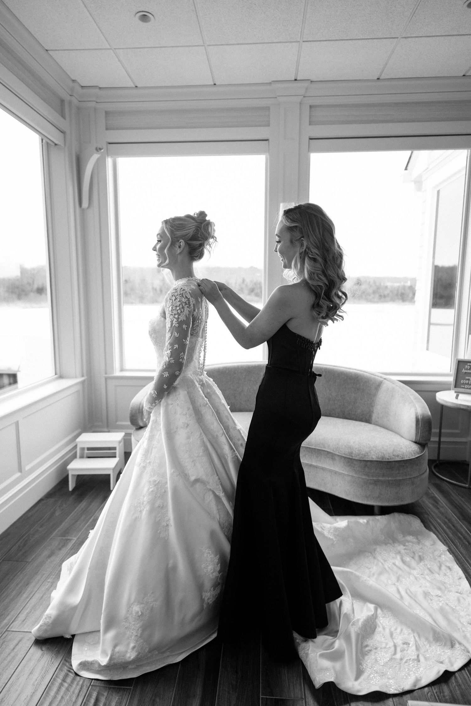 Black and white photo of wedding dress preparation in sunlit room.