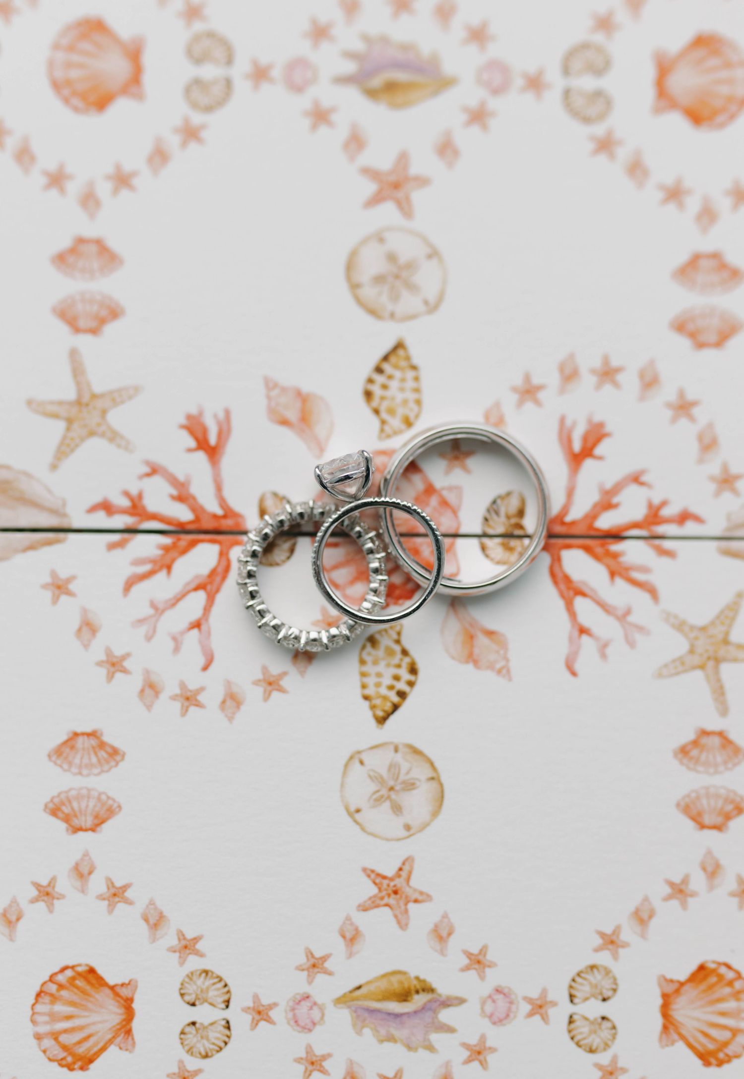 Wedding rings arranged on coral and seashell patterned paper.